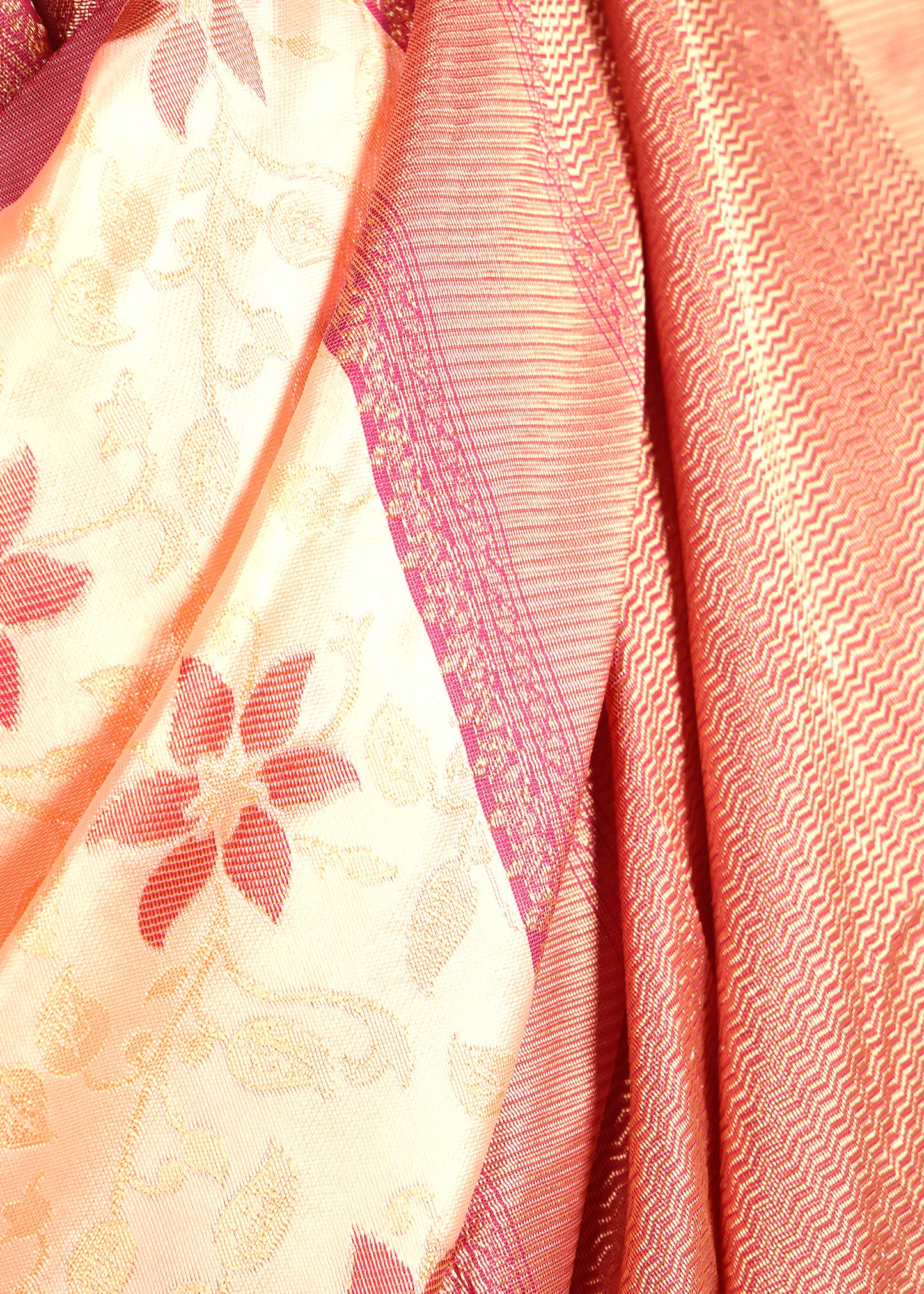 Close-up of a peach silk saree with gold zari and floral motifs, highlighting the fine craftsmanship.