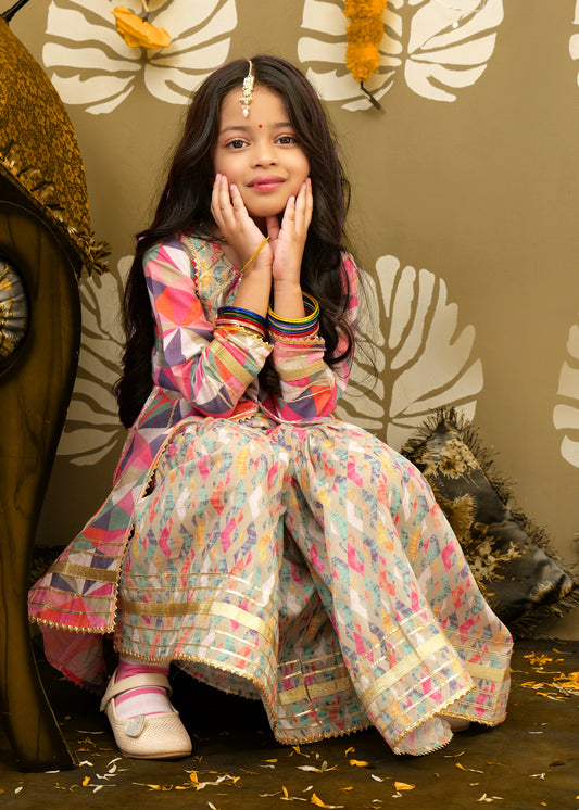 A young girl in a playful pose, dressed in a colorful ethnic kurta and floral palazzo set, showcasing the intricate design and bright colors, ideal for festive celebrations.