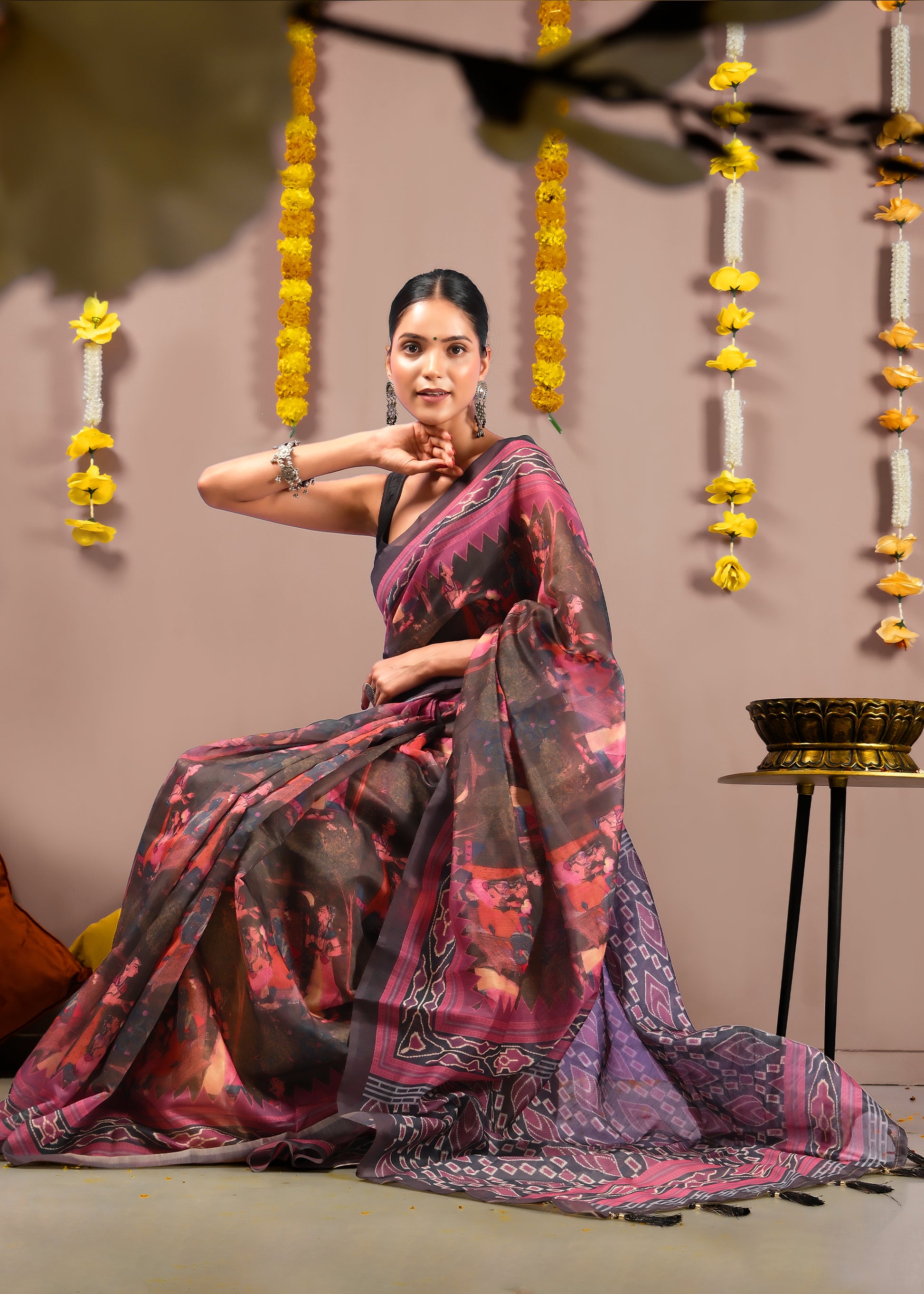 Woman sitting elegantly, displaying the Krishna Rasleela scenes and bold Ikat patterns on her saree.