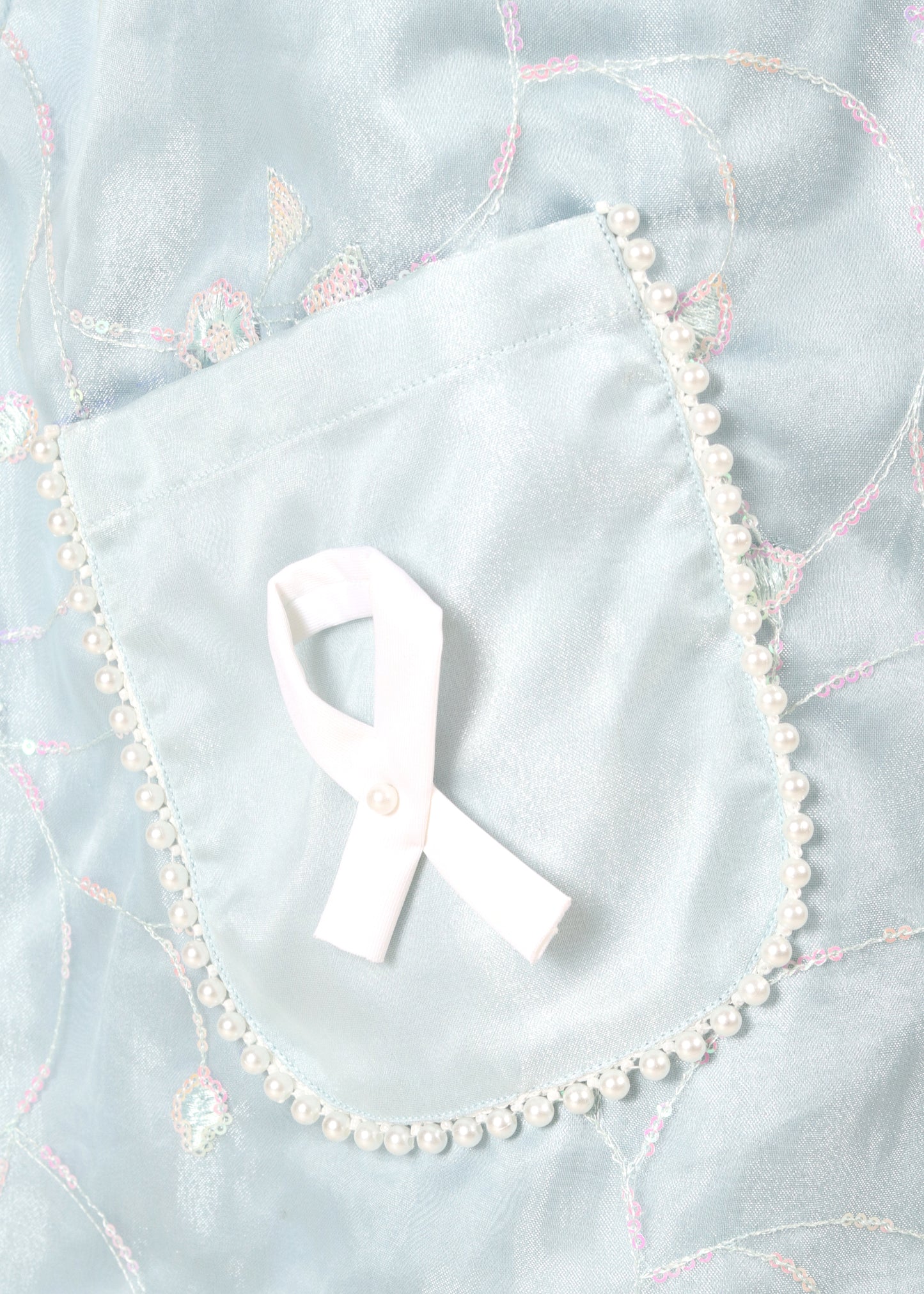 Close-up of a light blue dress pocket with a white ribbon detail and pearl embellishments, highlighting the delicate embroidery work