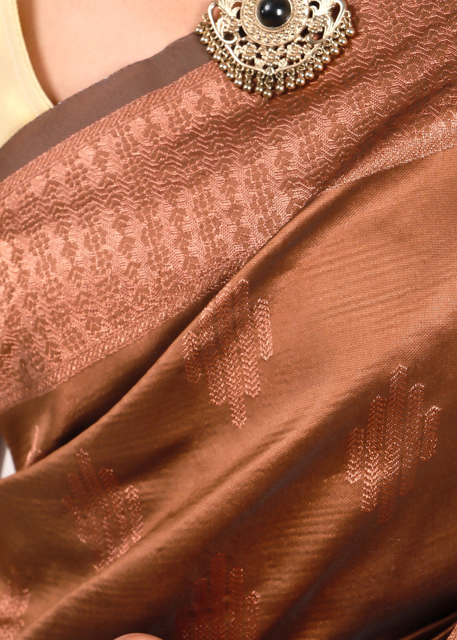 Close-up of the brown silk saree’s delicate woven detailing, highlighting the intricate design and fabric texture