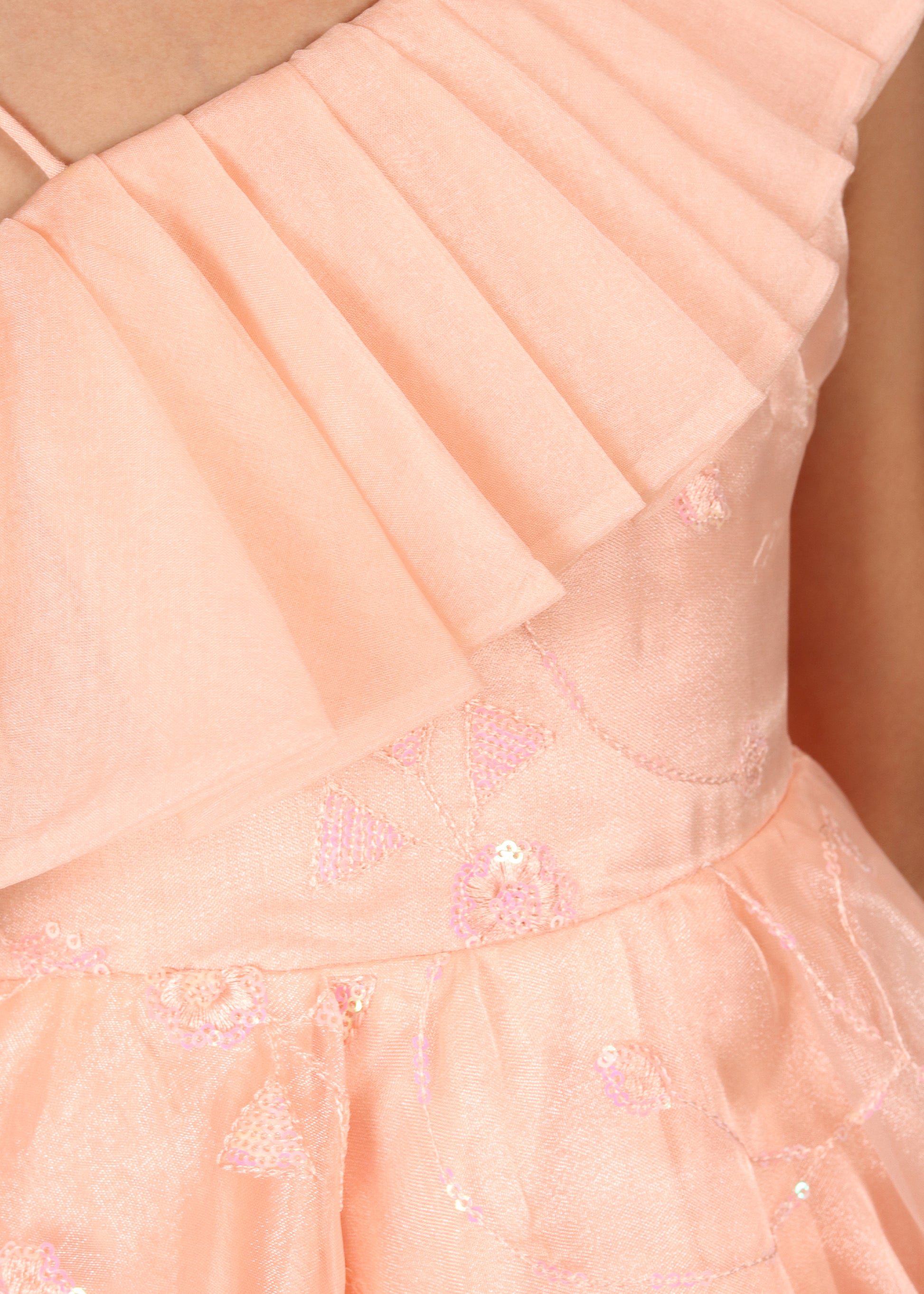 "Close-up of the peach one-shoulder dress, showcasing the pleated ruffle detail on the shoulder and the intricate floral embroidery on the bodice."