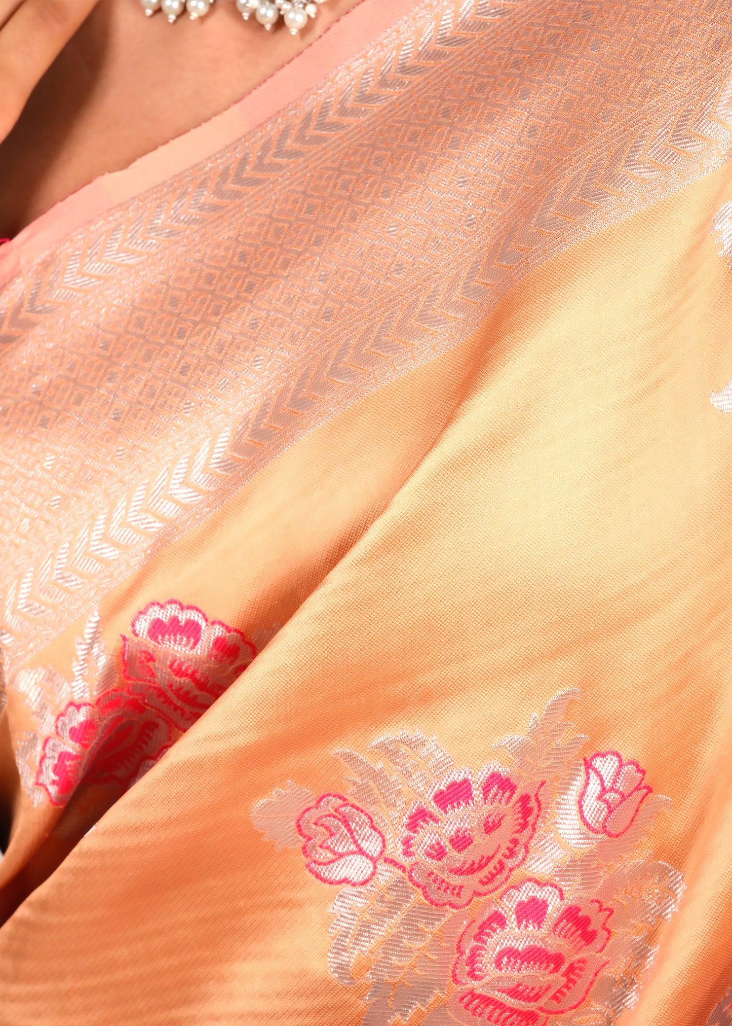 Close-up of a peach-colored Banarasi silk saree showcasing detailed pink floral embroidery and silver zari design