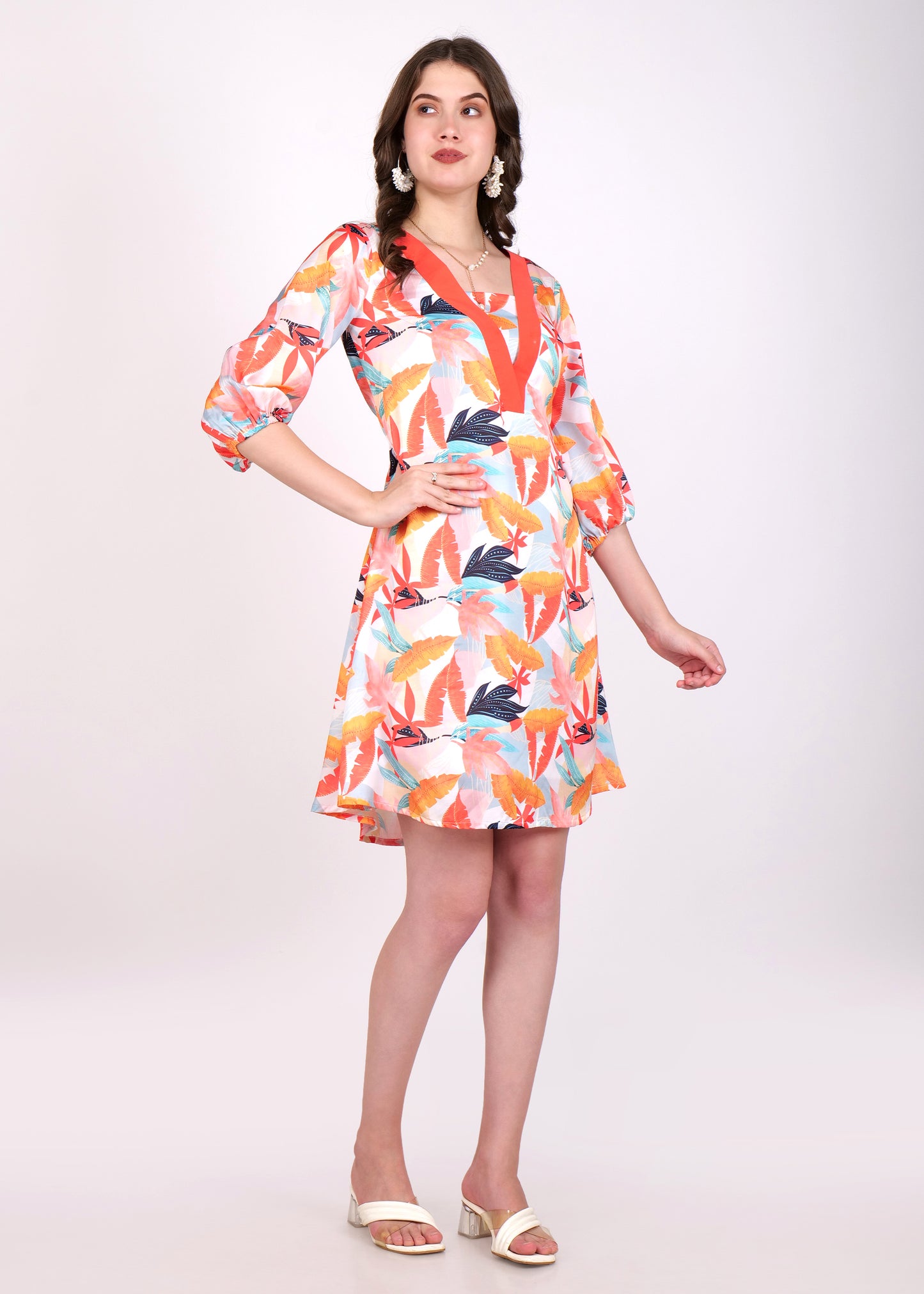 A woman wearing a colorful floral-print V-neck dress with a bold orange border. The dress has three-quarter sleeves and a flowing A-line cut