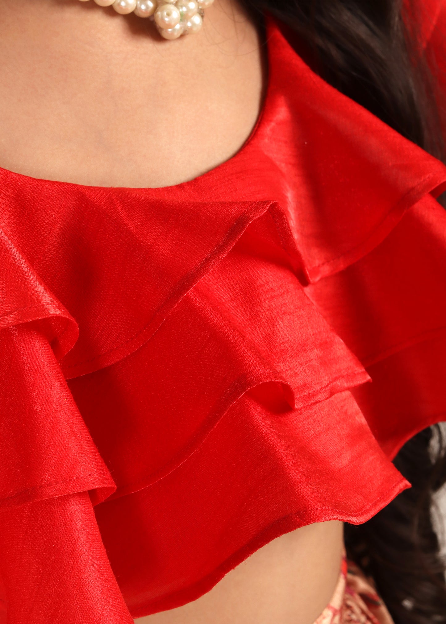 Close-up of a red ruffled crop top with fine details, styled with a pearl necklace for an elegant, festive look.