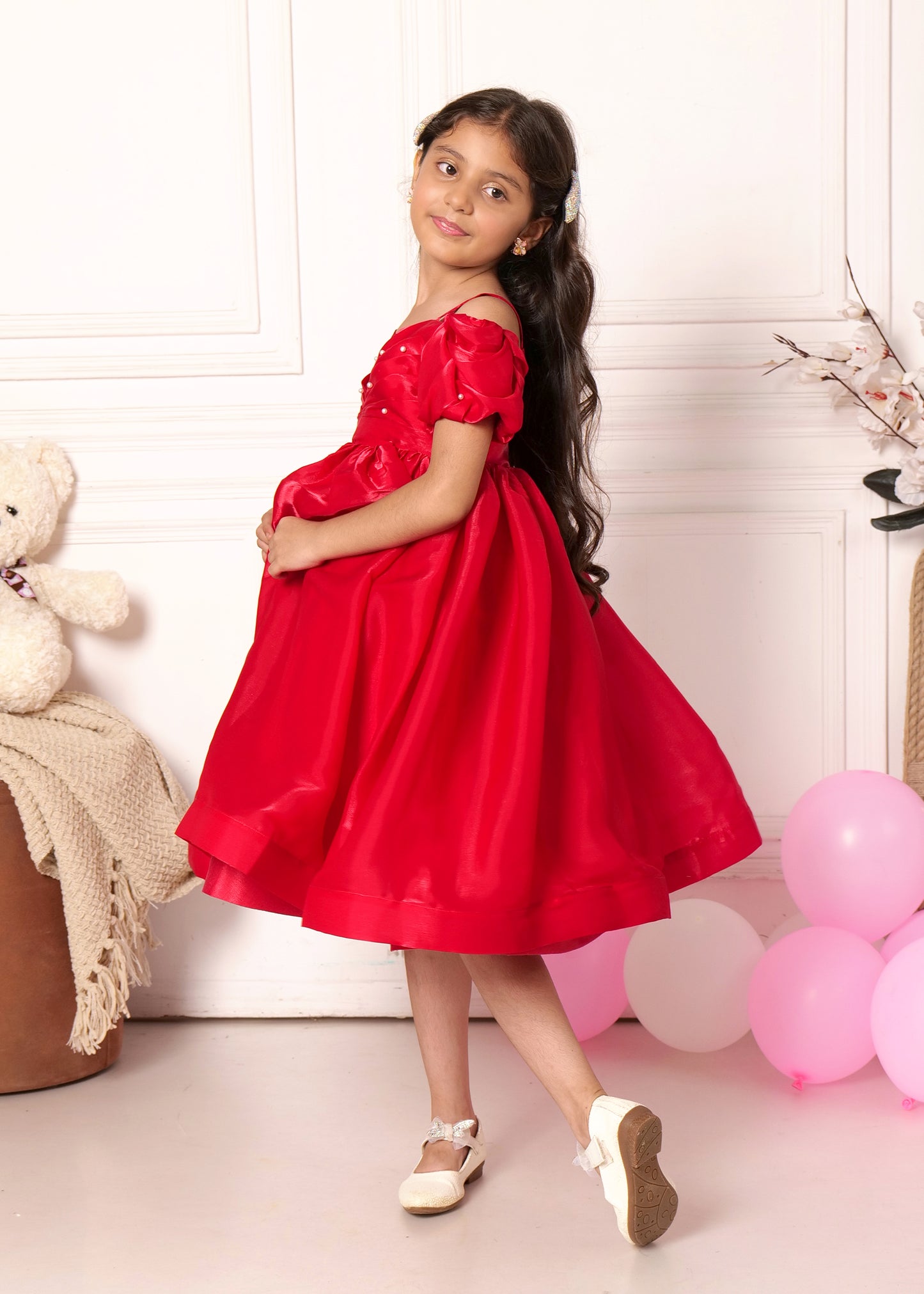 "Charming little girl twirling in a red satin puff-sleeve dress, showing off her outfit from a side angle, ideal for festive events or parties."