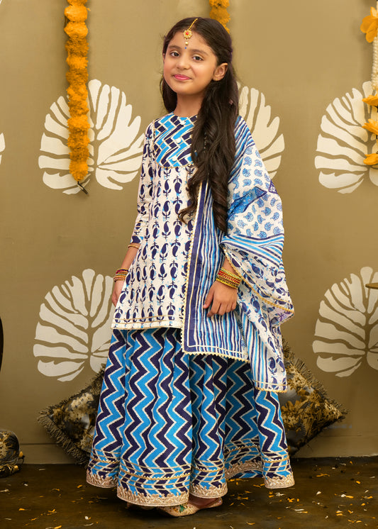 A young girl posing in a stylish blue and white ethnic kurta with intricate patterns, paired with a printed palazzo and dupatta, exuding a festive vibe.