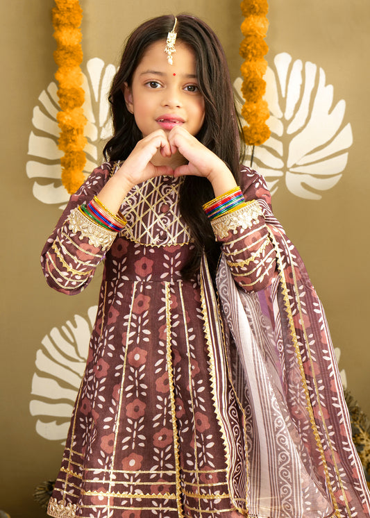 A young girl posing with a heart-shaped hand gesture, wearing a beautifully embroidered maroon kurta and palazzo set with gold accents. The ethnic attire is perfect for festivals and special occasions.