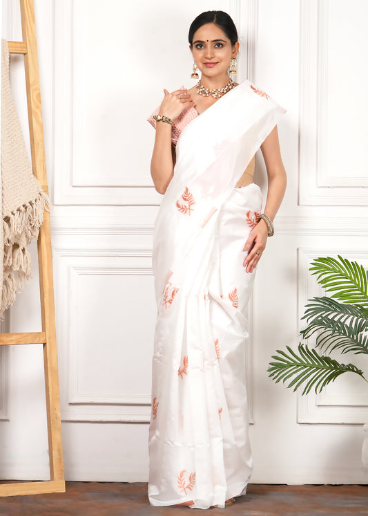 Model poses in a pristine white saree adorned with orange floral embroidery and a matching blouse, exuding elegance and charm