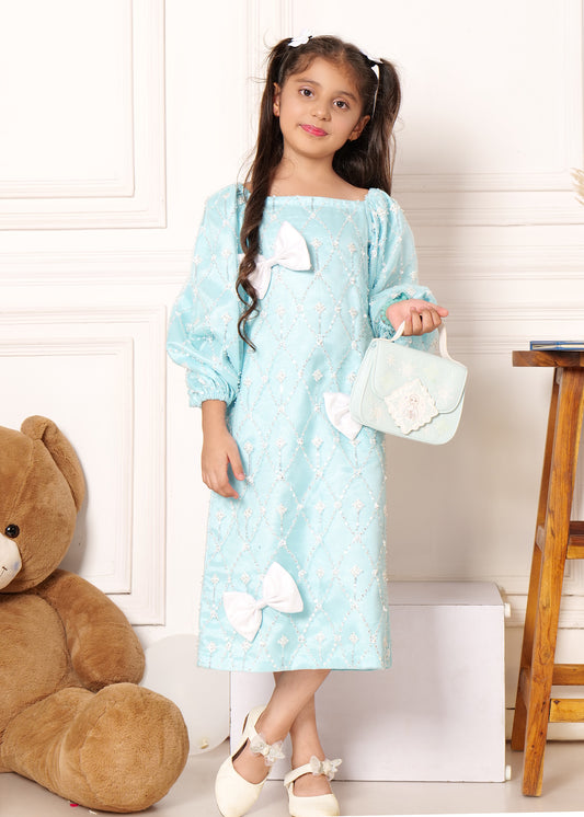 Young model dressed in a light blue dress adorned with bows and pearls, holding a handbag, ideal for formal children’s wear photoshoots