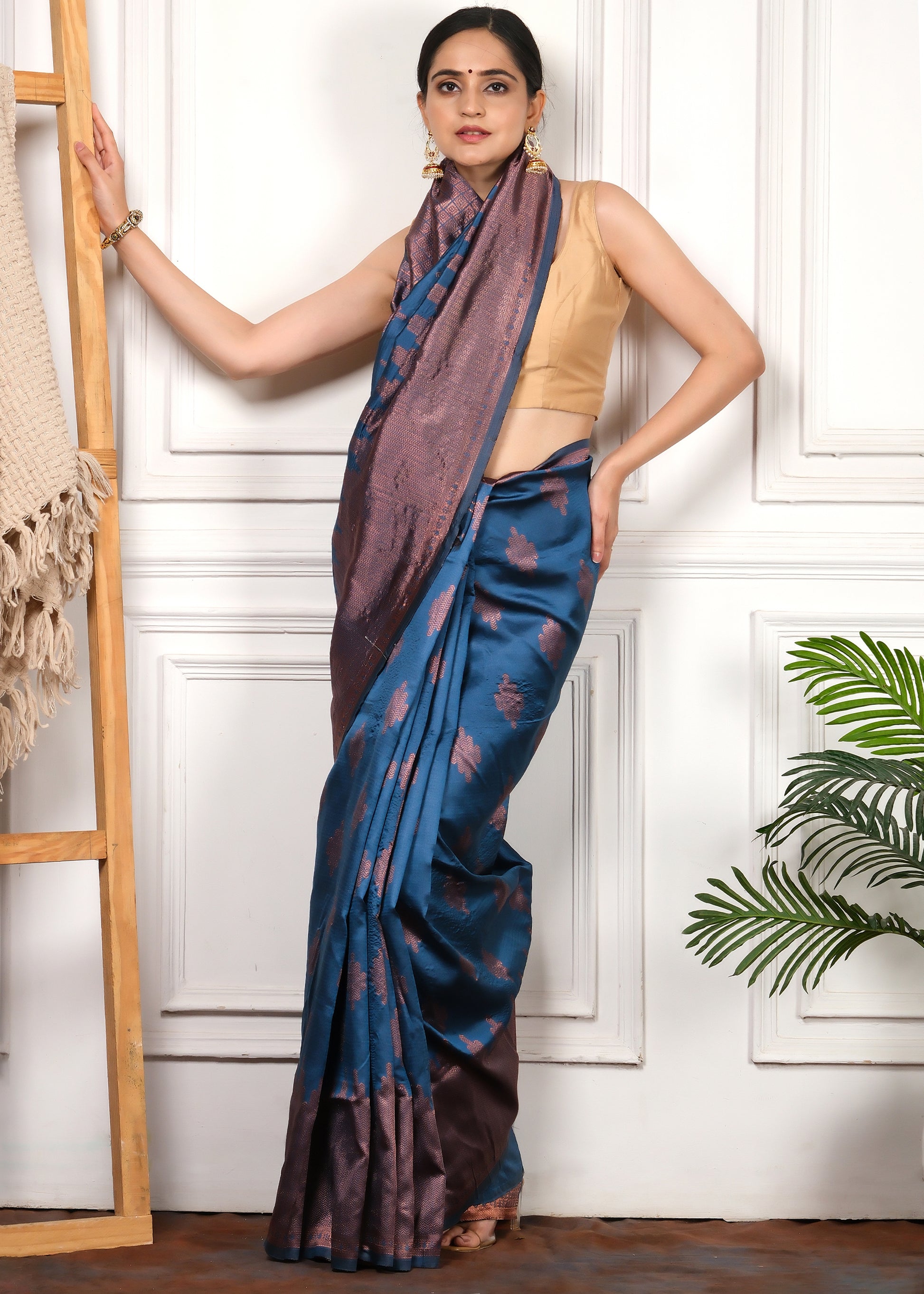 Full-length view of model posing in a royal blue and copper woven silk saree against a traditional backdrop