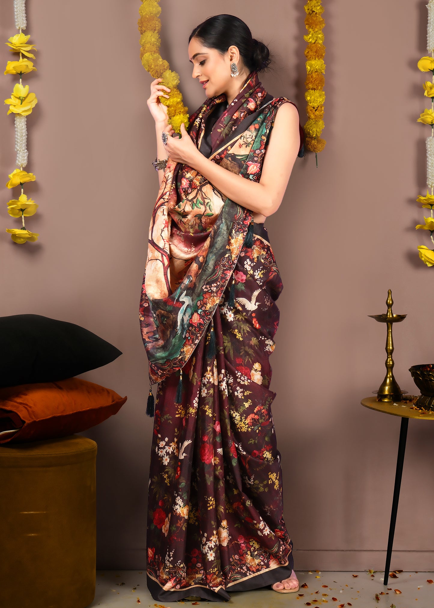 Model holding yellow flowers while wearing a maroon saree with intricate floral designs, styled for a festive look