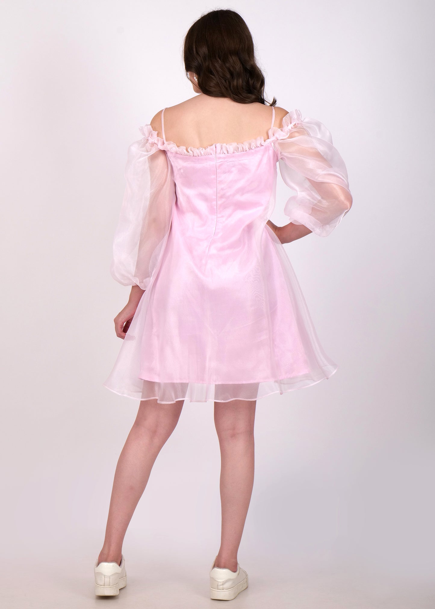 "Back view of a woman in a pink off-shoulder mini dress with sheer puffed sleeves and ruffle detailing."