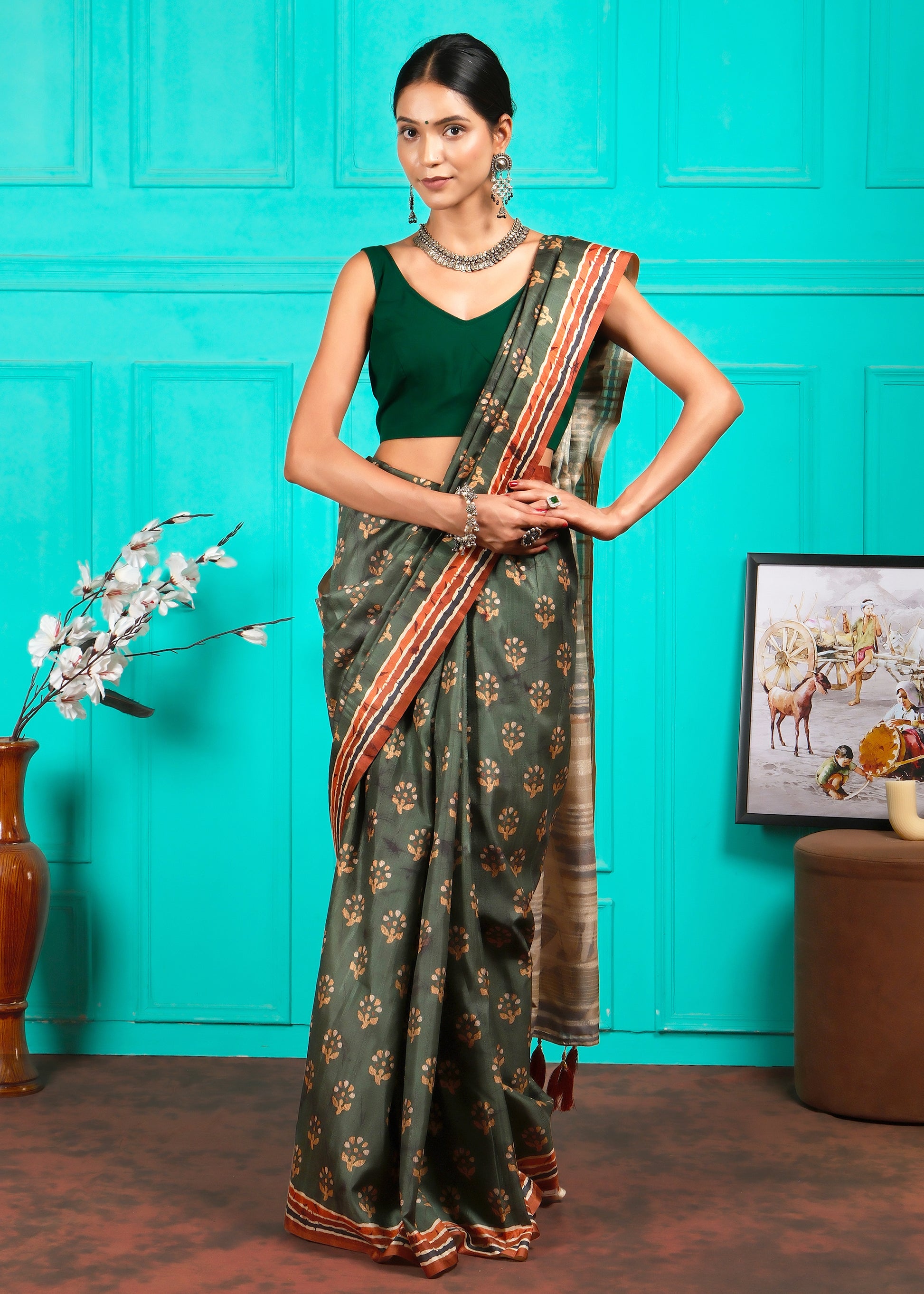 Model posing in a traditional green saree with golden motifs, in a vibrant turquoise room setting