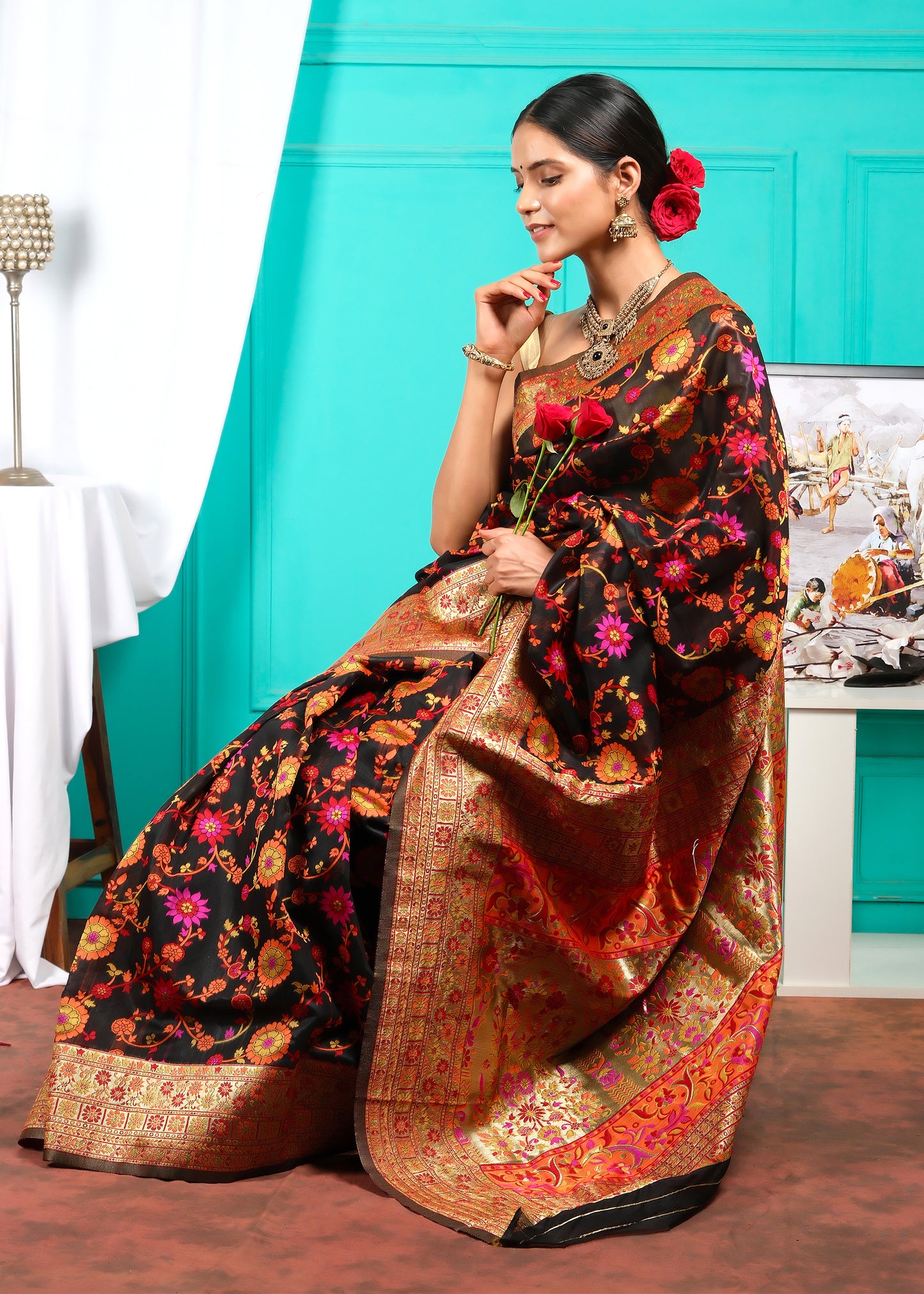 Seated model in black Banarasi silk saree with rich floral patterns and gold zari pallu, ideal for festive celebrations