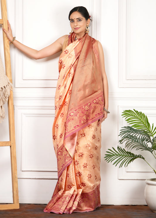 Woman posing in a peach silk saree with a contrast gold and pink border, adding a touch of luxury to her look