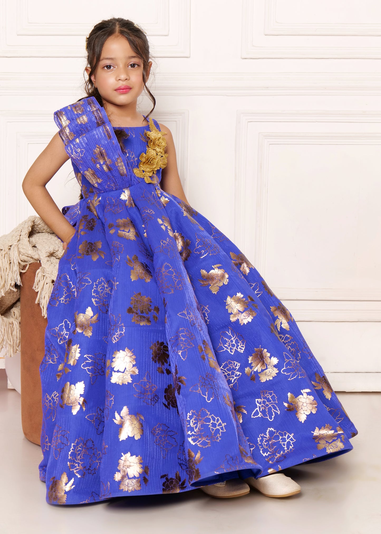 Young girl sitting elegantly in a royal blue dress with intricate gold floral patterns, a charming outfit for formal occasions