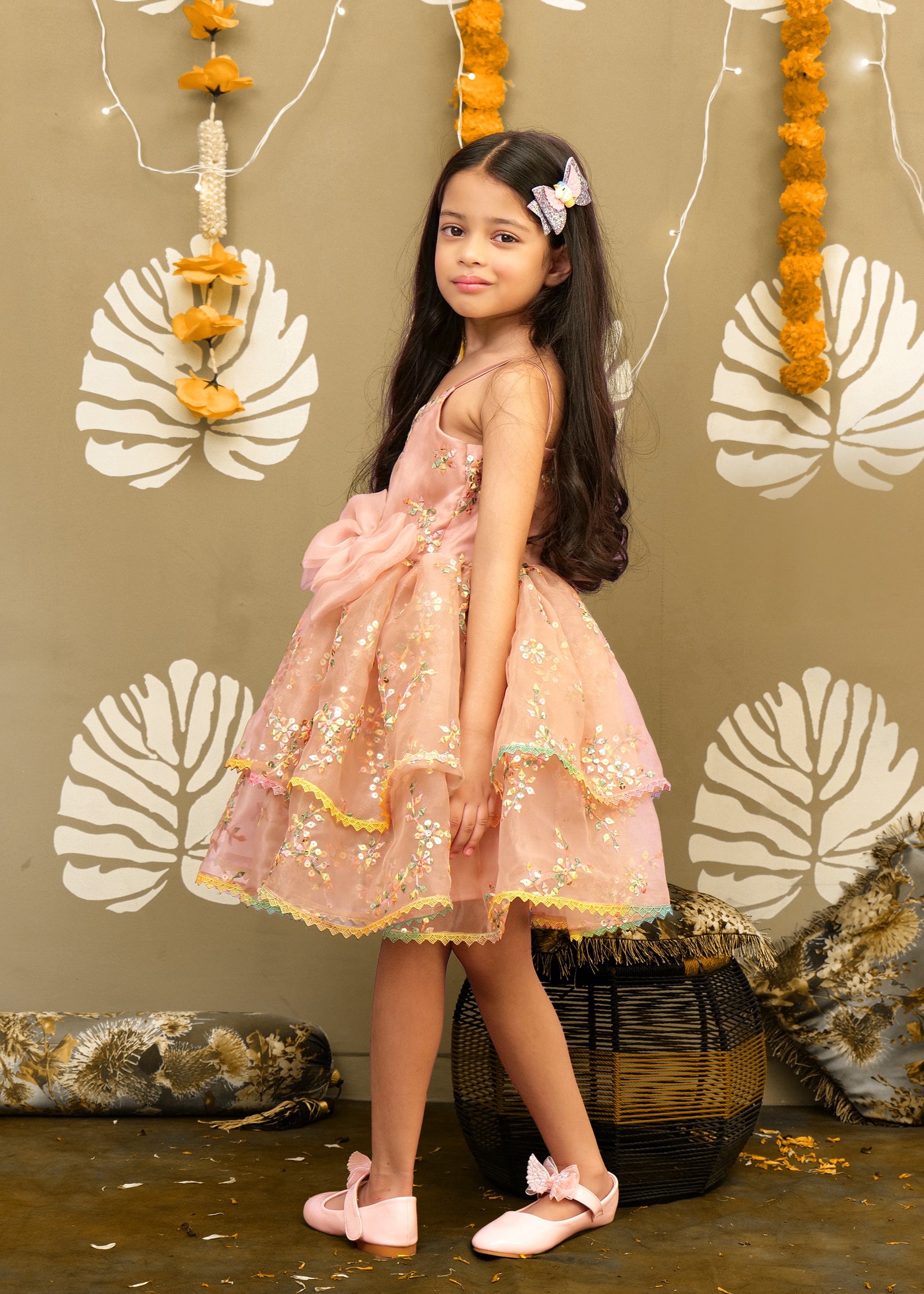 Side view of a young girl in a peach floral dress with a big bow, showing off her elegant outfit with a flowy skirt.