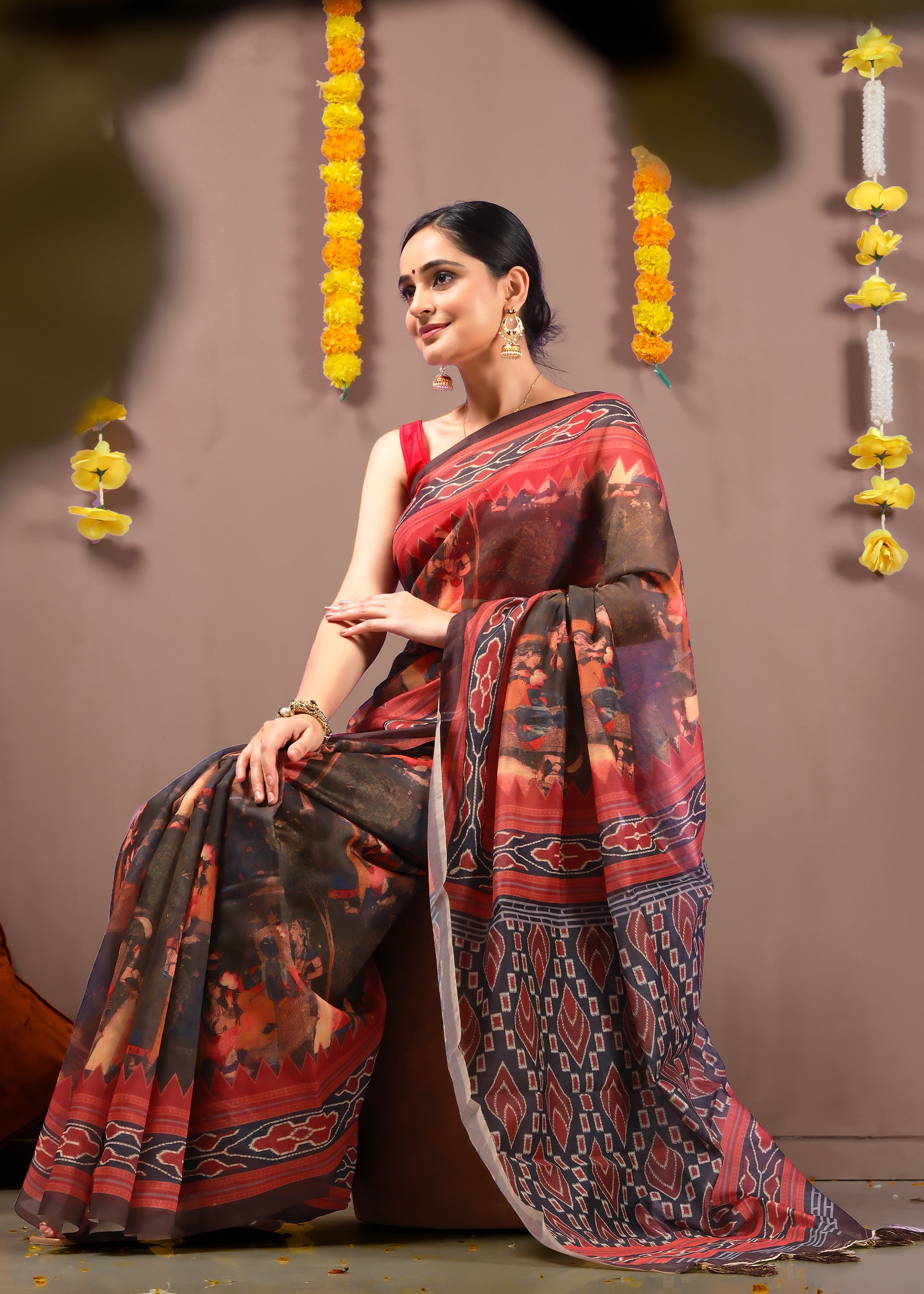 Woman sitting elegantly in a traditional Ikat saree with bold red and black geometric designs.