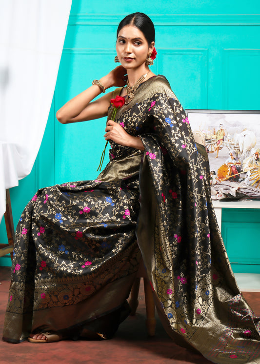 Model elegantly draped in a black Banarasi saree, sitting gracefully, showcasing the vibrant floral design on a gold zari backdrop