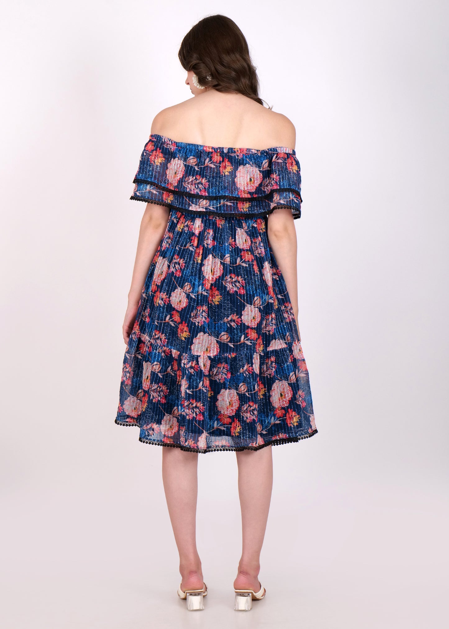 Back view of a navy blue floral pleated off-shoulder midi dress, showcasing tiered ruffles and black lace trim, worn by a woman with white heels.
Image 5: Close-up of a navy blue floral pleated dress f