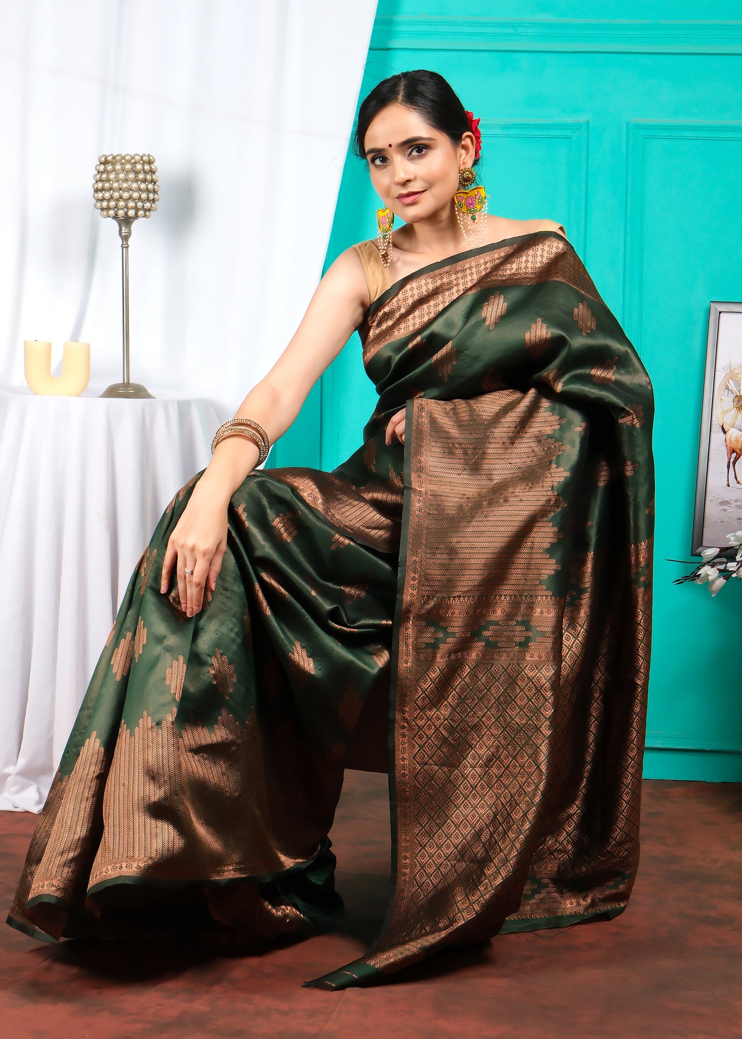 Woman sitting gracefully in a traditional green and brown silk saree with golden patterns.