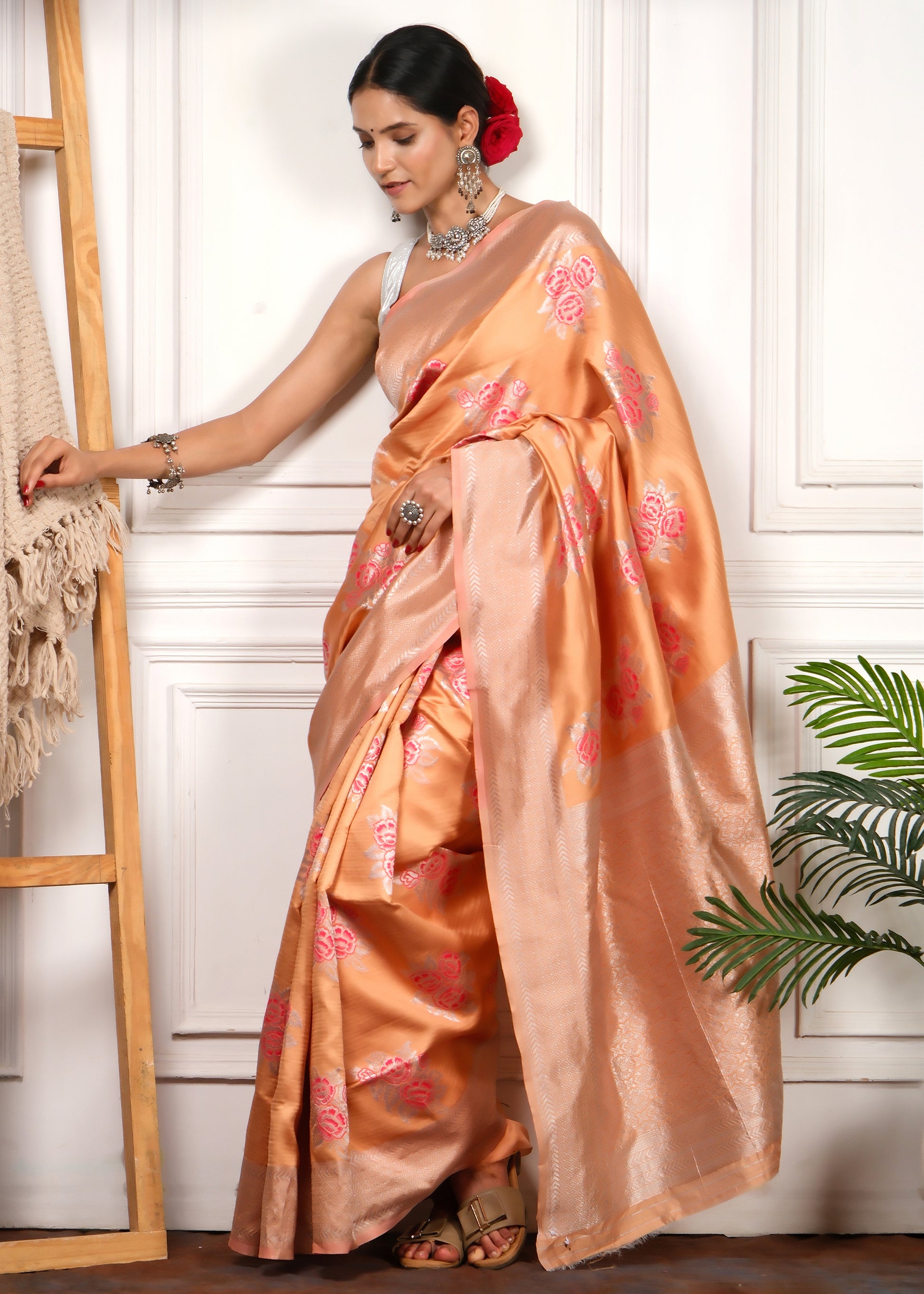 Front view of a model in a peach-colored Banarasi silk saree with silver zari and pink floral designs, ideal for festive occasions