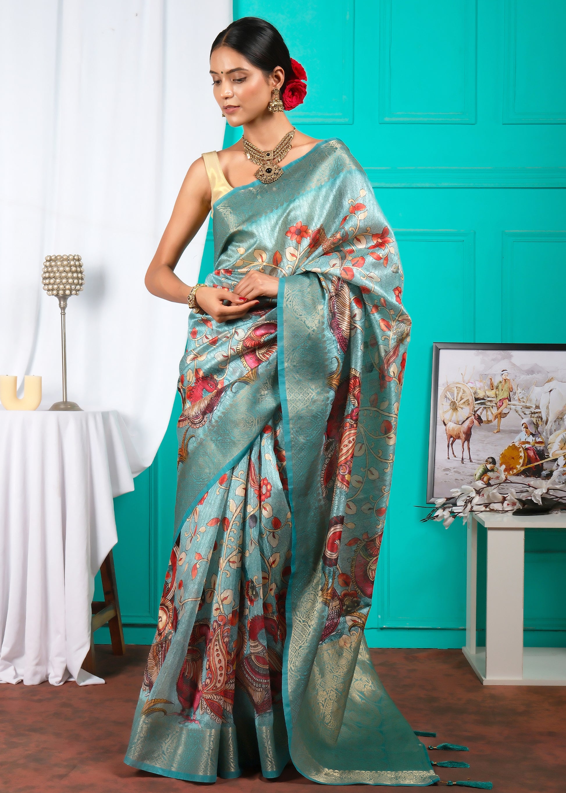 Side view of a teal silk saree with detailed floral and peacock artwork, perfect for traditional occasions, modeled gracefully in a vintage-inspired setting.