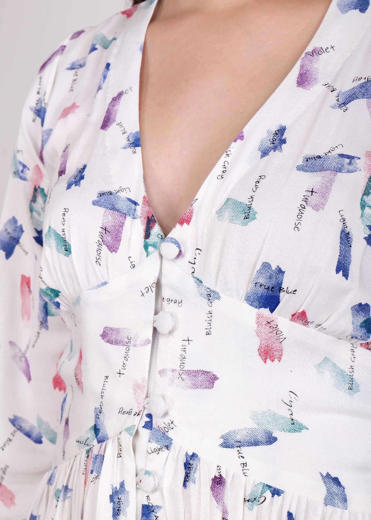 close view of Woman wearing a white knee-length dress with a floral print, featuring bell sleeves and a deep V-neckline