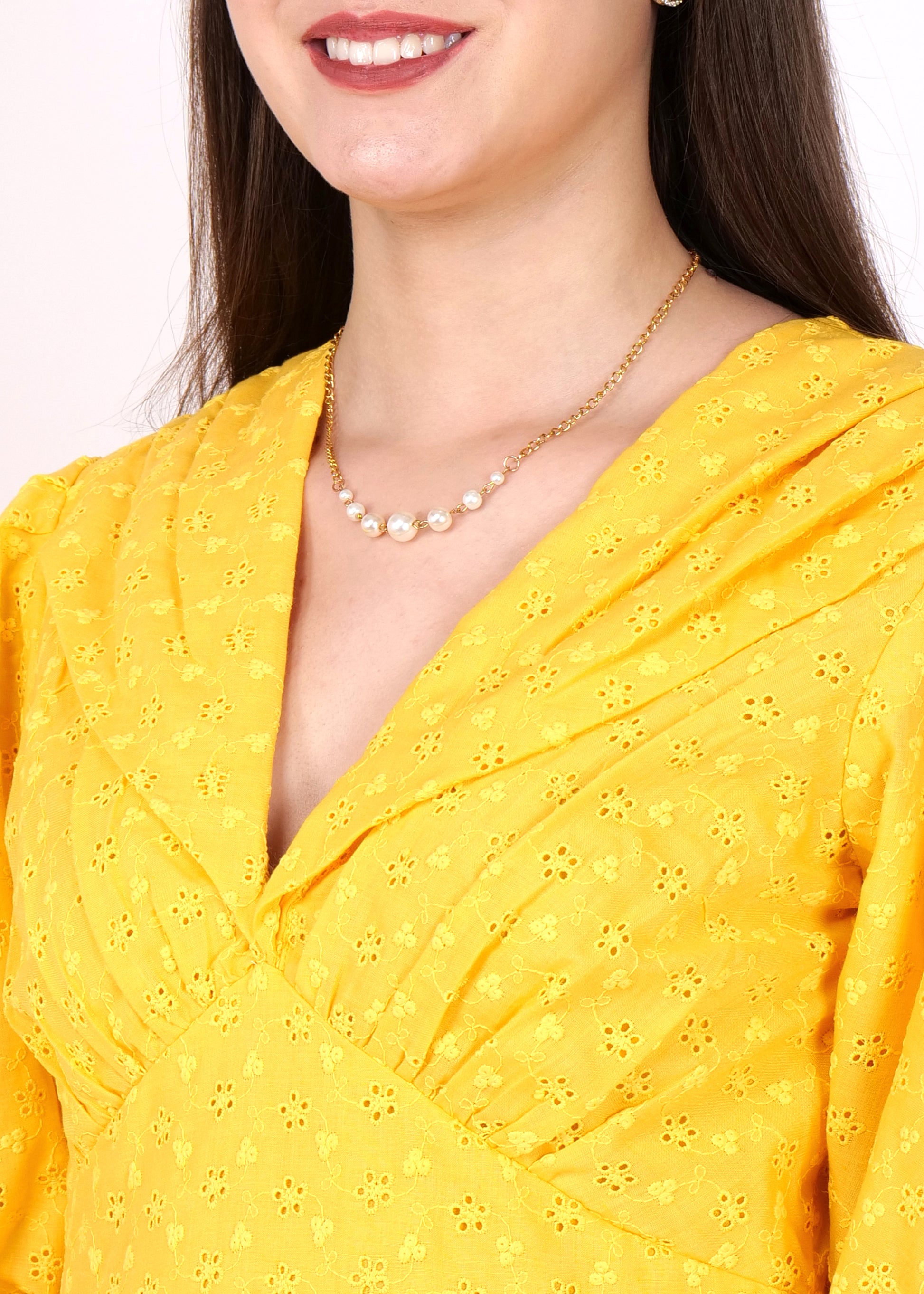 Close-up of the neckline of a yellow dress with intricate embroidery details, paired with a pearl necklace for an elegant touch