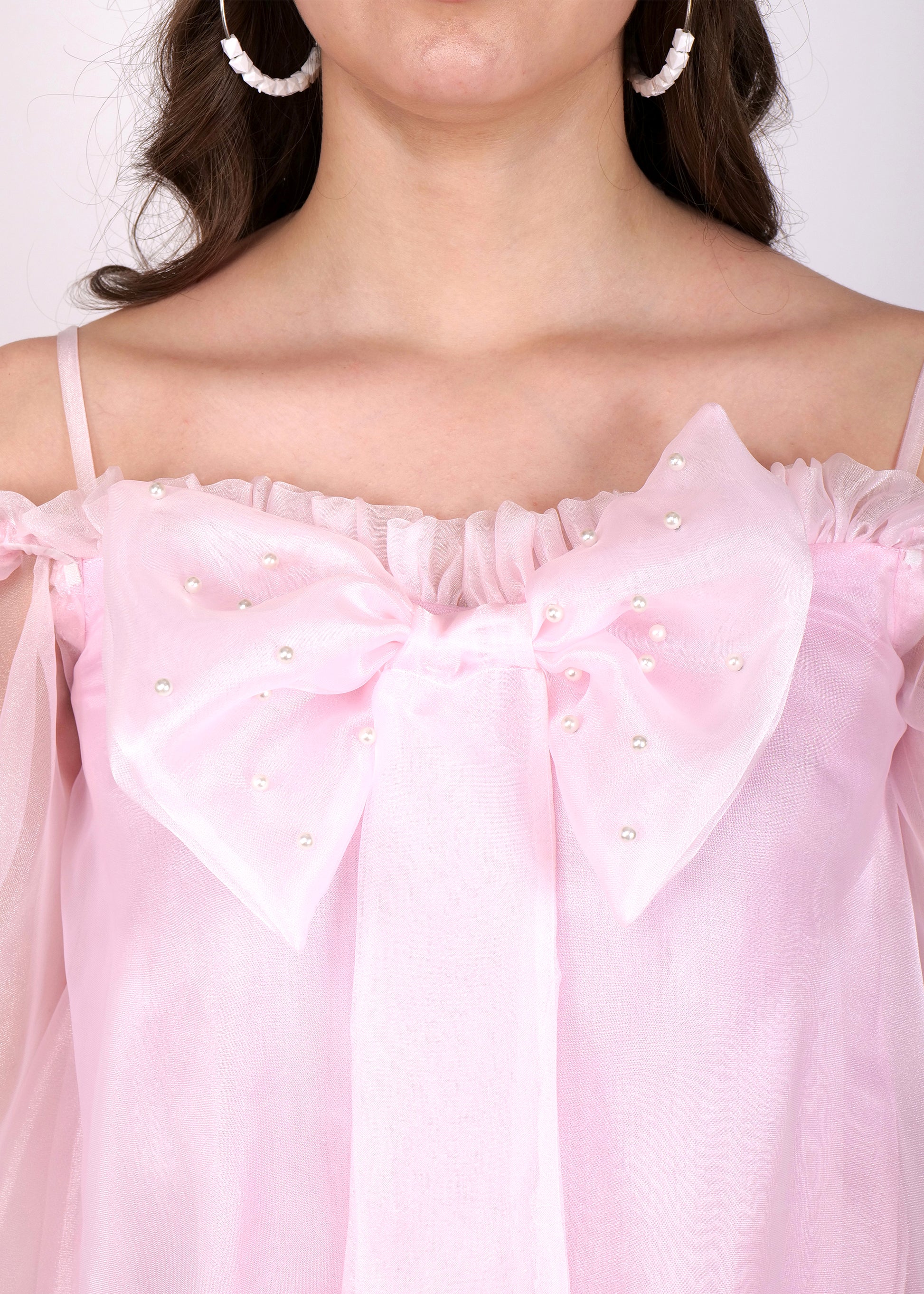 "Close-up of pink off-shoulder dress showing bow and pearl detailing at the neckline."