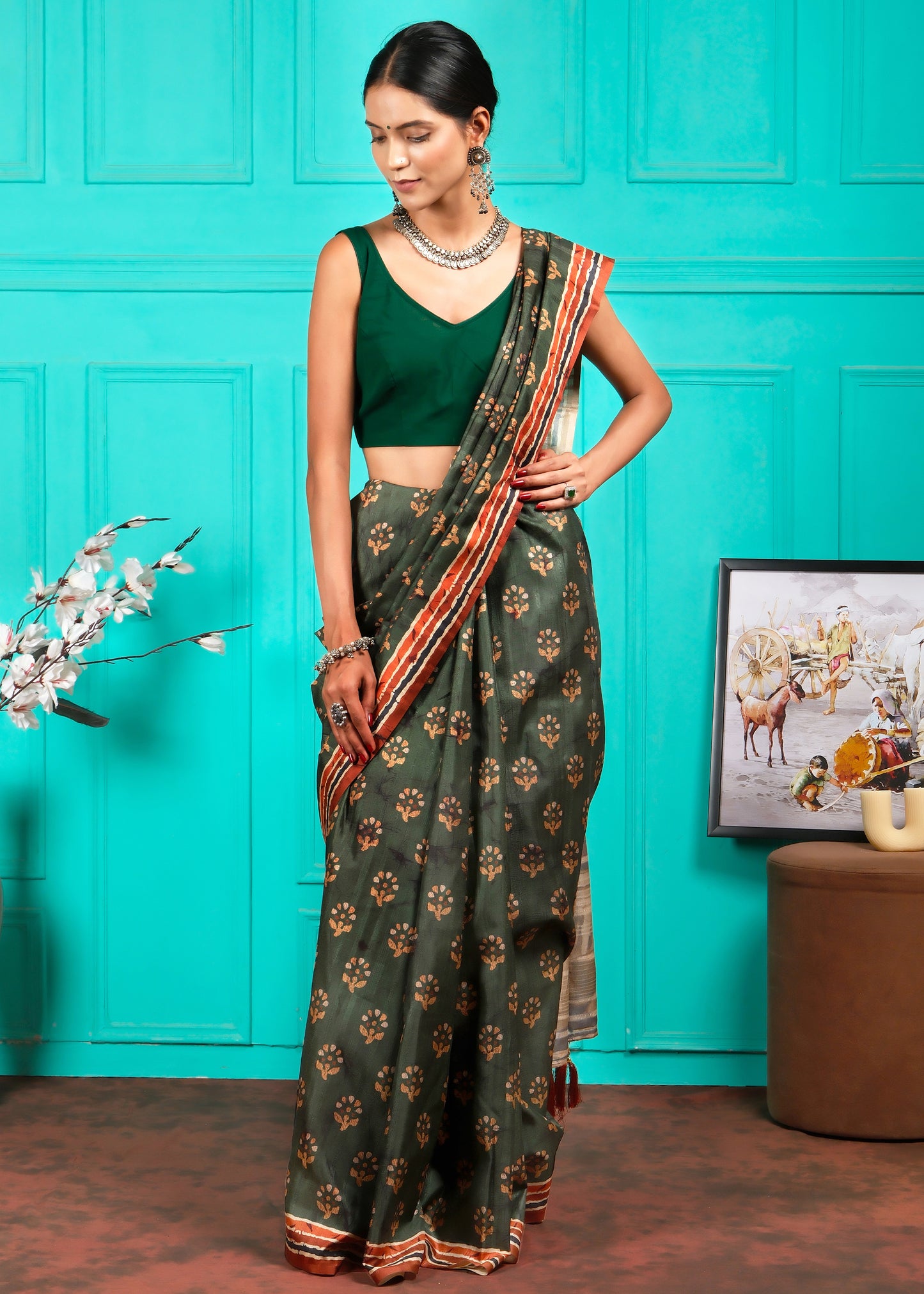 Elegant model in a green saree, standing in a traditional setting, highlighting its bold print and tassel details