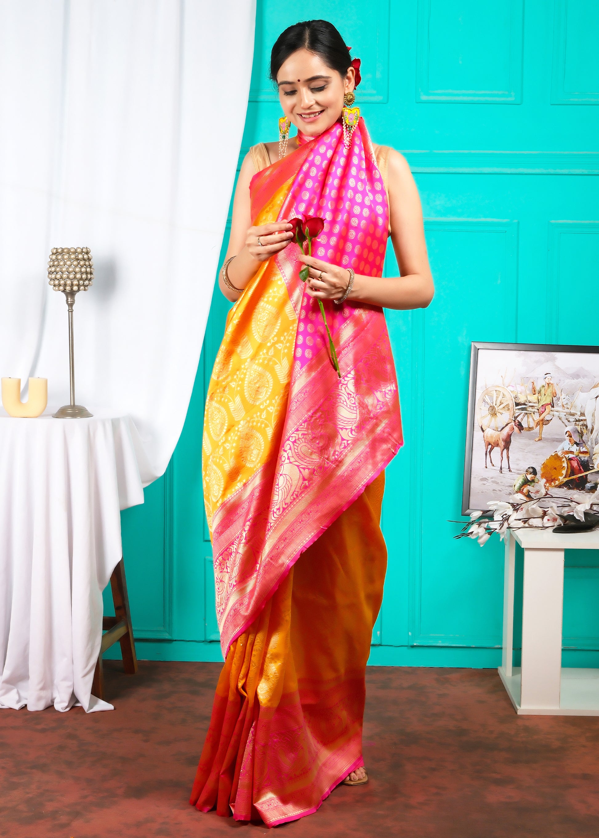 Side view of a model in a bright orange and pink silk saree with detailed golden patterns, posed gracefully against a turquoise backdrop