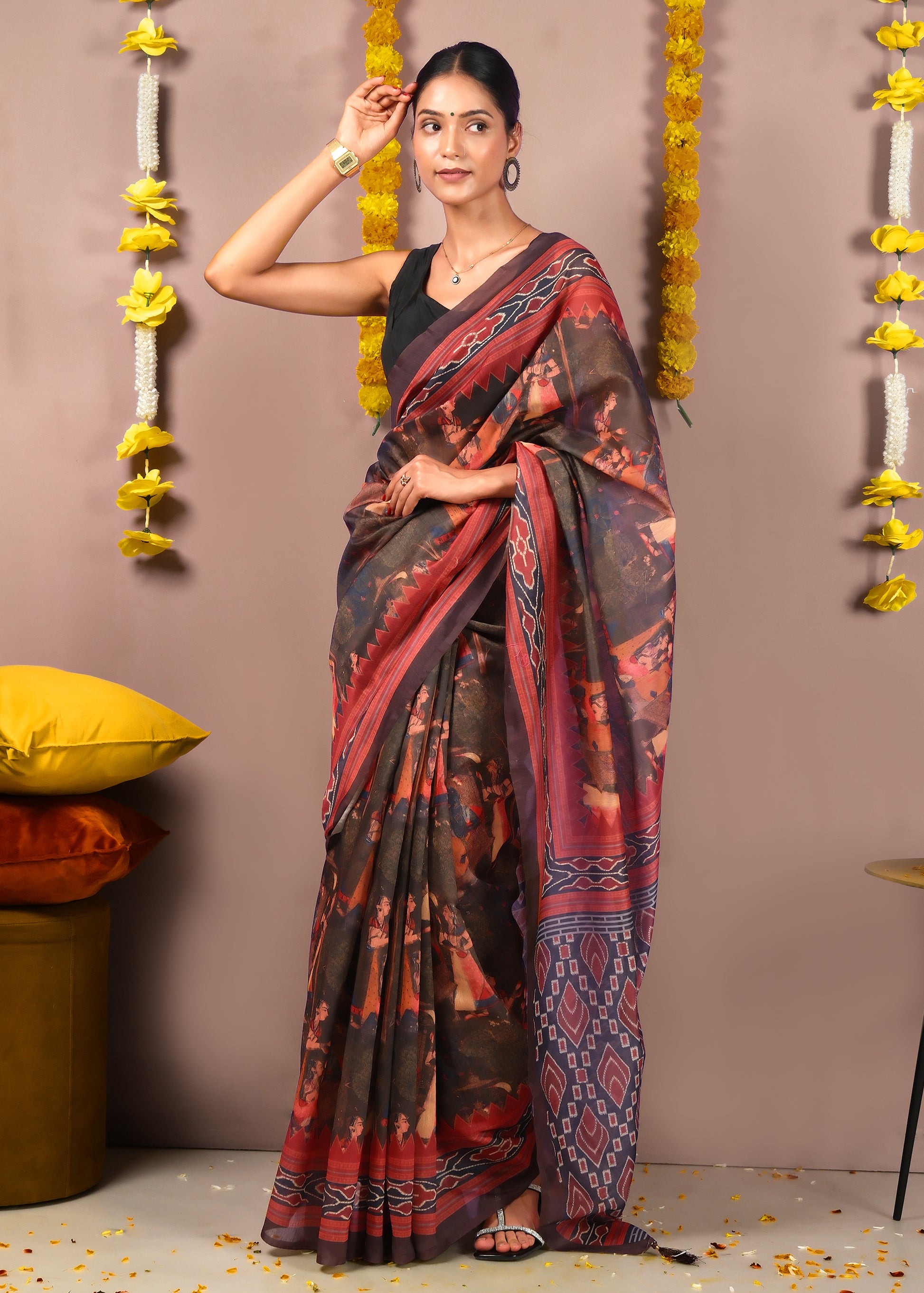 Woman seated in a red and black saree featuring traditional cultural patterns, styled for a special occasion or ceremony.