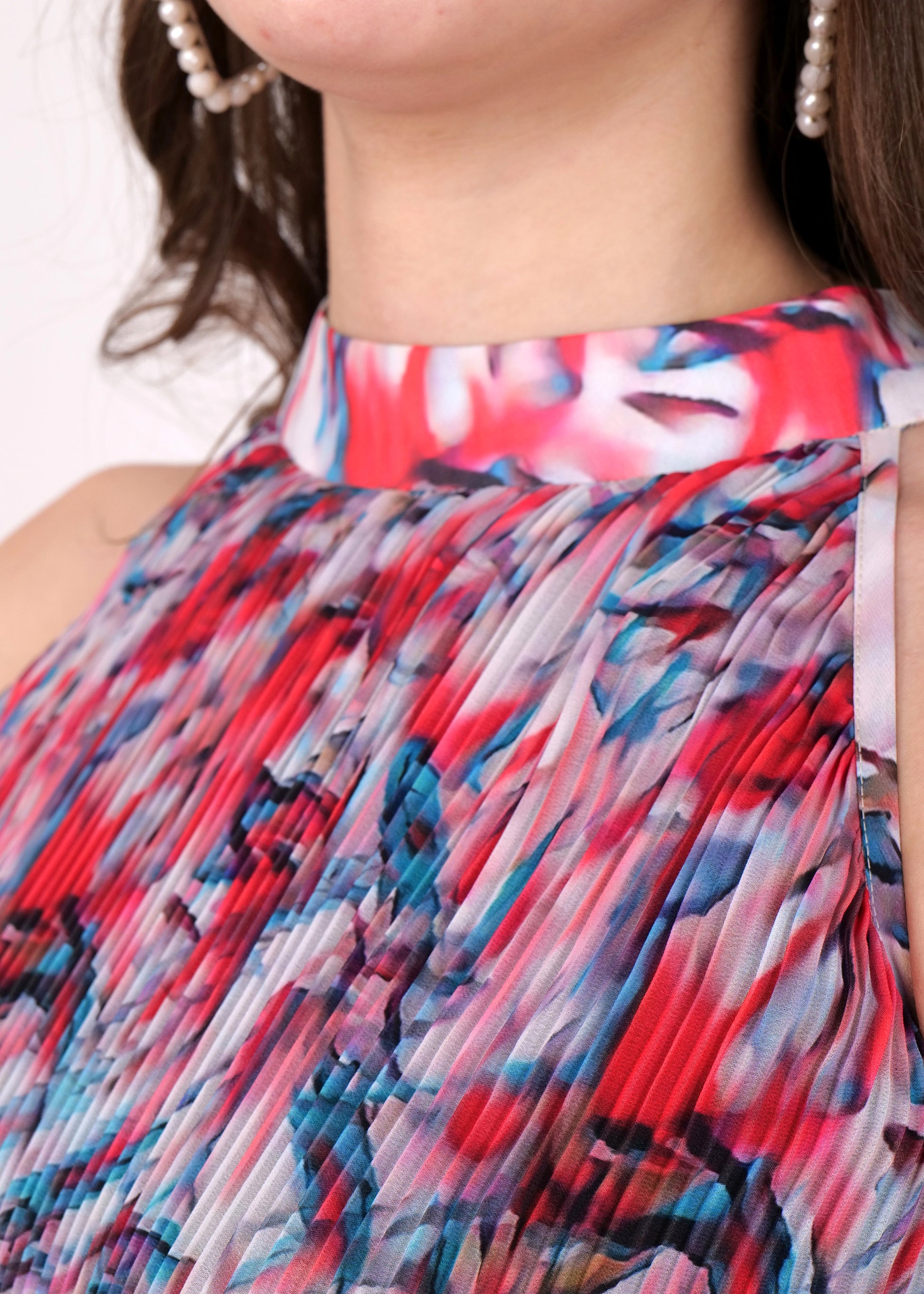 Close-up of the high-neck pleated midi dress, highlighting the red and blue abstract print fabric.