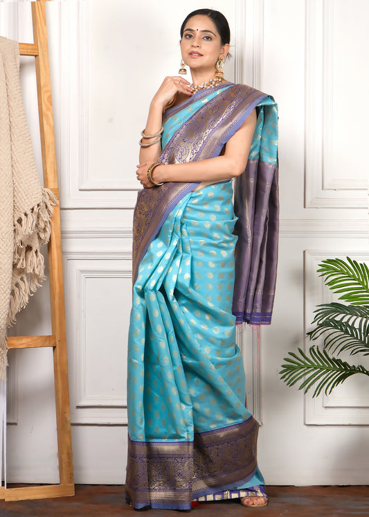 Woman gracefully posing in a turquoise blue silk saree with a gold zari border, paired with bangles and earrings for a perfect ethnic look.