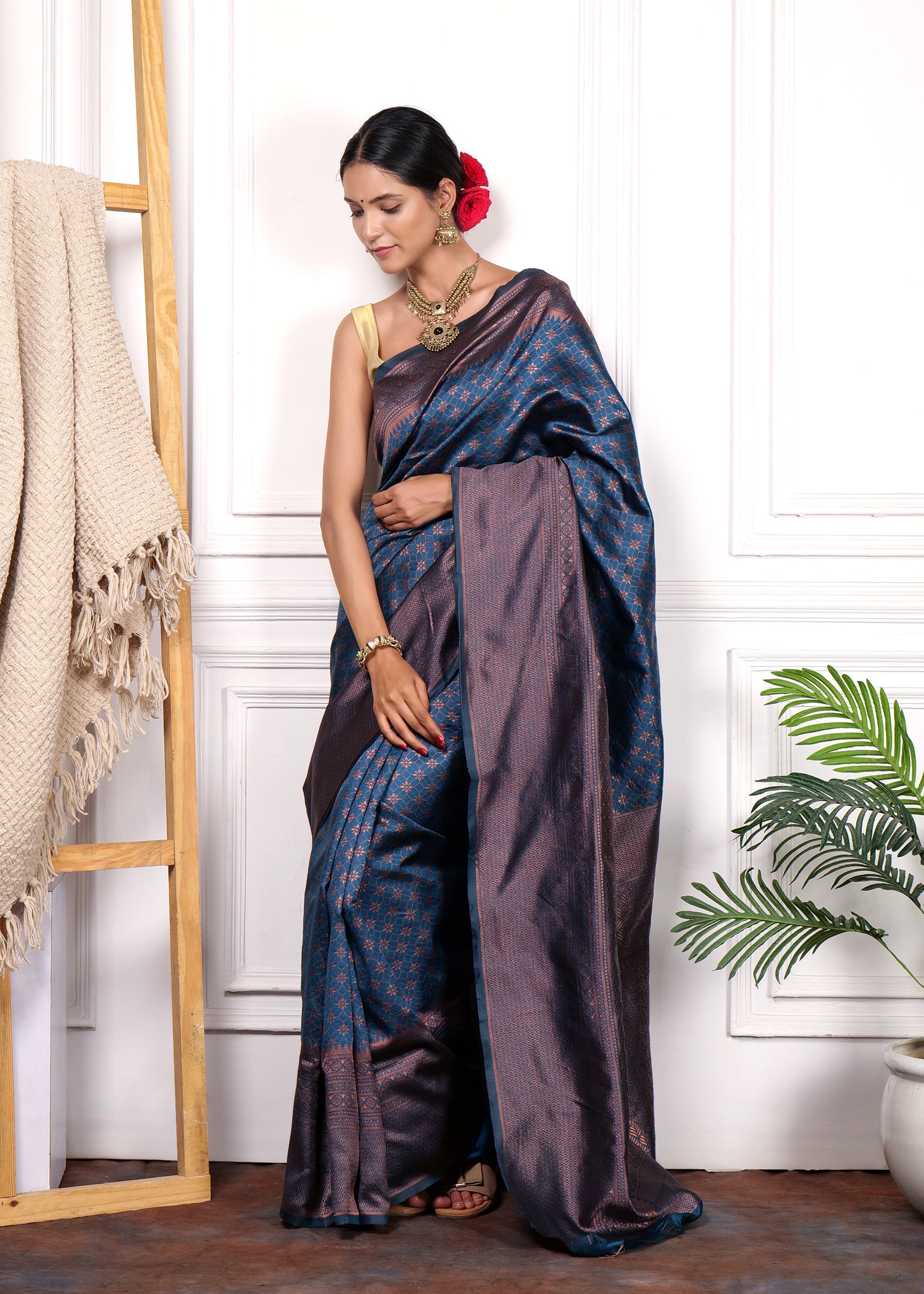 Full view of woman in navy blue Kanjivaram silk saree, featuring intricate copper motifs, styled with red rose hair accessories