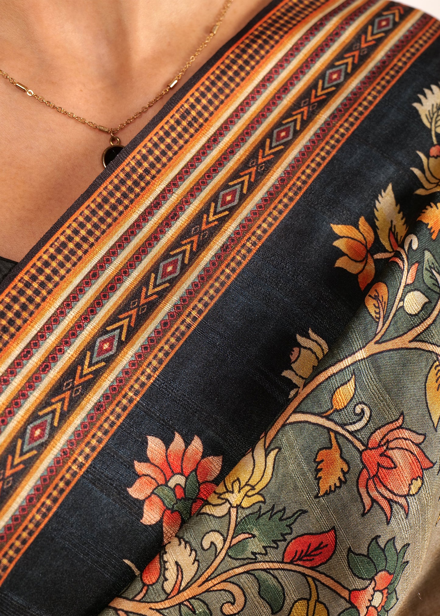 Close-up of saree’s border showcasing detailed floral embroidery and geometric patterns on a black background.
