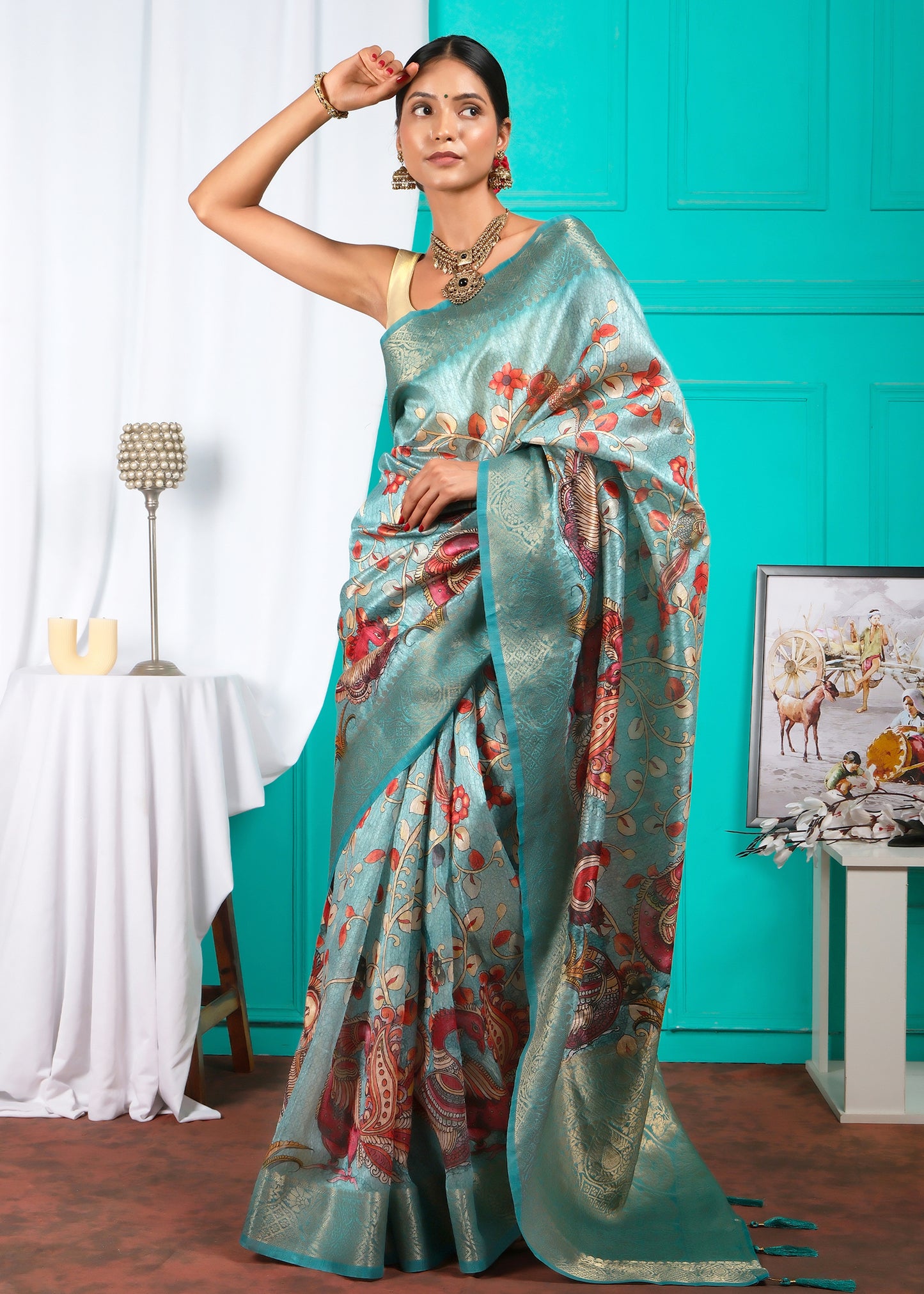 Model adorned in a teal saree with intricate peacock motifs, paired with gold jewelry and red flowers in her hair, capturing the essence of Indian tradition.