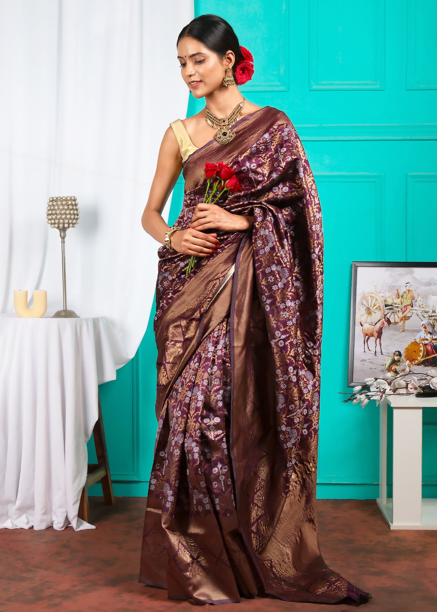 The model elegantly adjusting her maroon saree with intricate gold details, standing with poise and confidence in a traditional setting