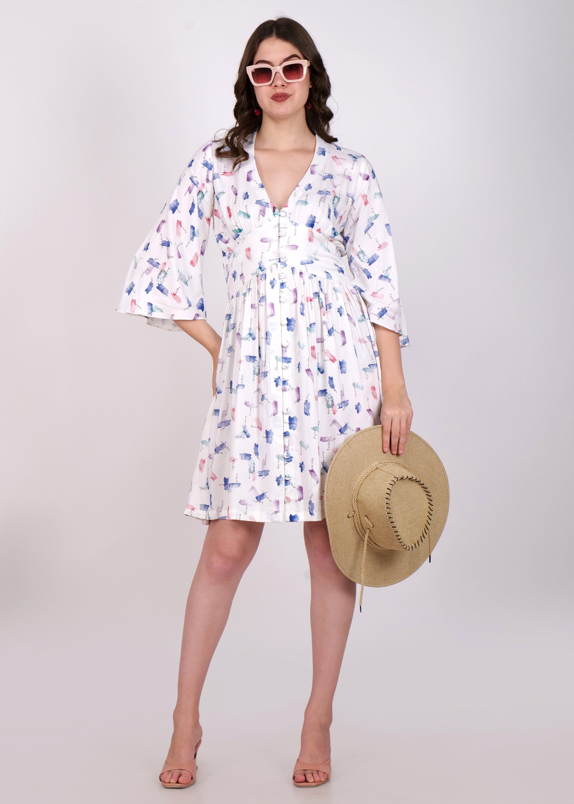 Woman in a white floral printed dress, accessorized with sunglasses and a straw hat, posing with a casual chic look