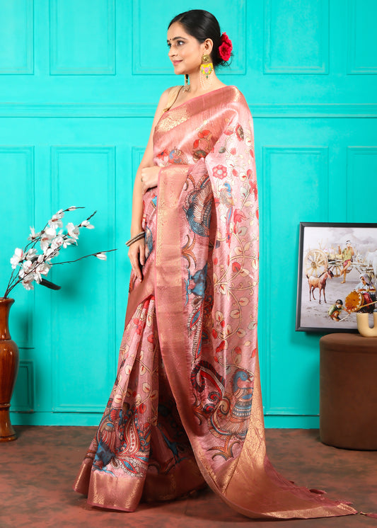 Woman adorned in a pink silk saree with delicate gold work and colorful motifs, posing with flowers in her hair and radiant accessories