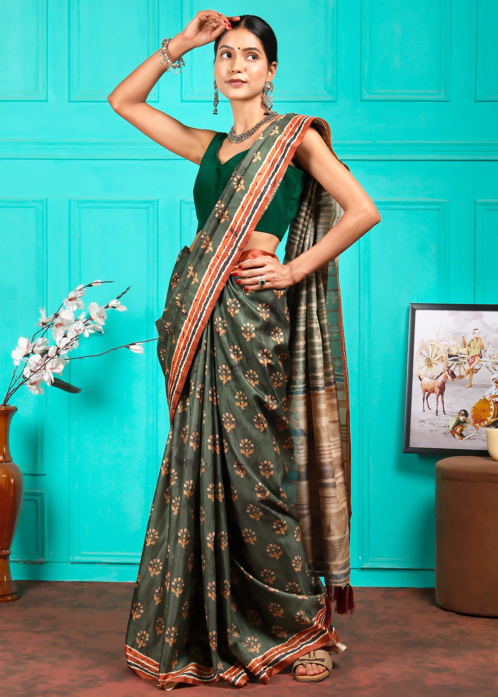 Model gracefully standing in a green saree with intricate golden floral motifs and a contrasting pallu.