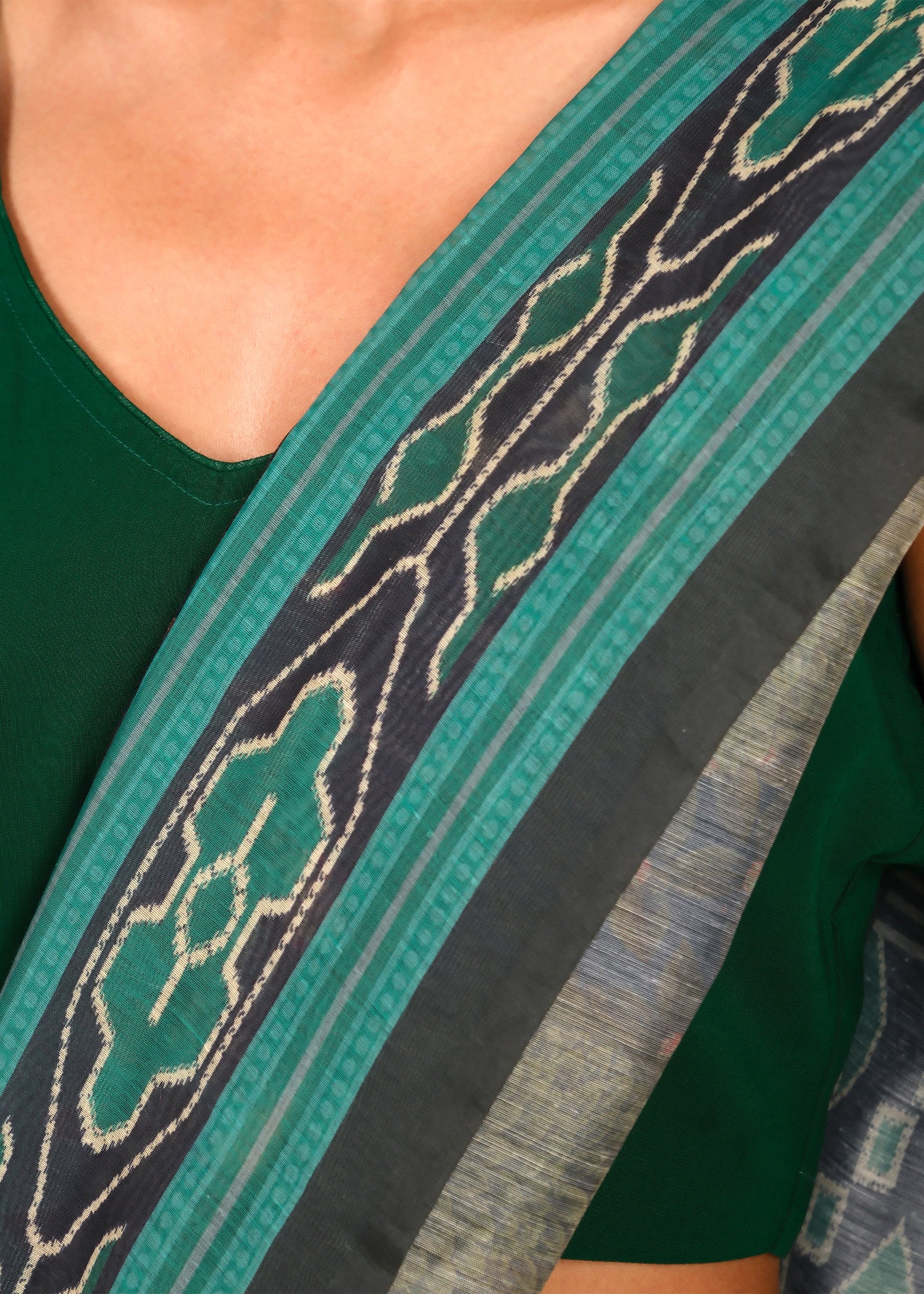 Close-up of a green saree border with traditional black and green designs worn by a model in a green blouse