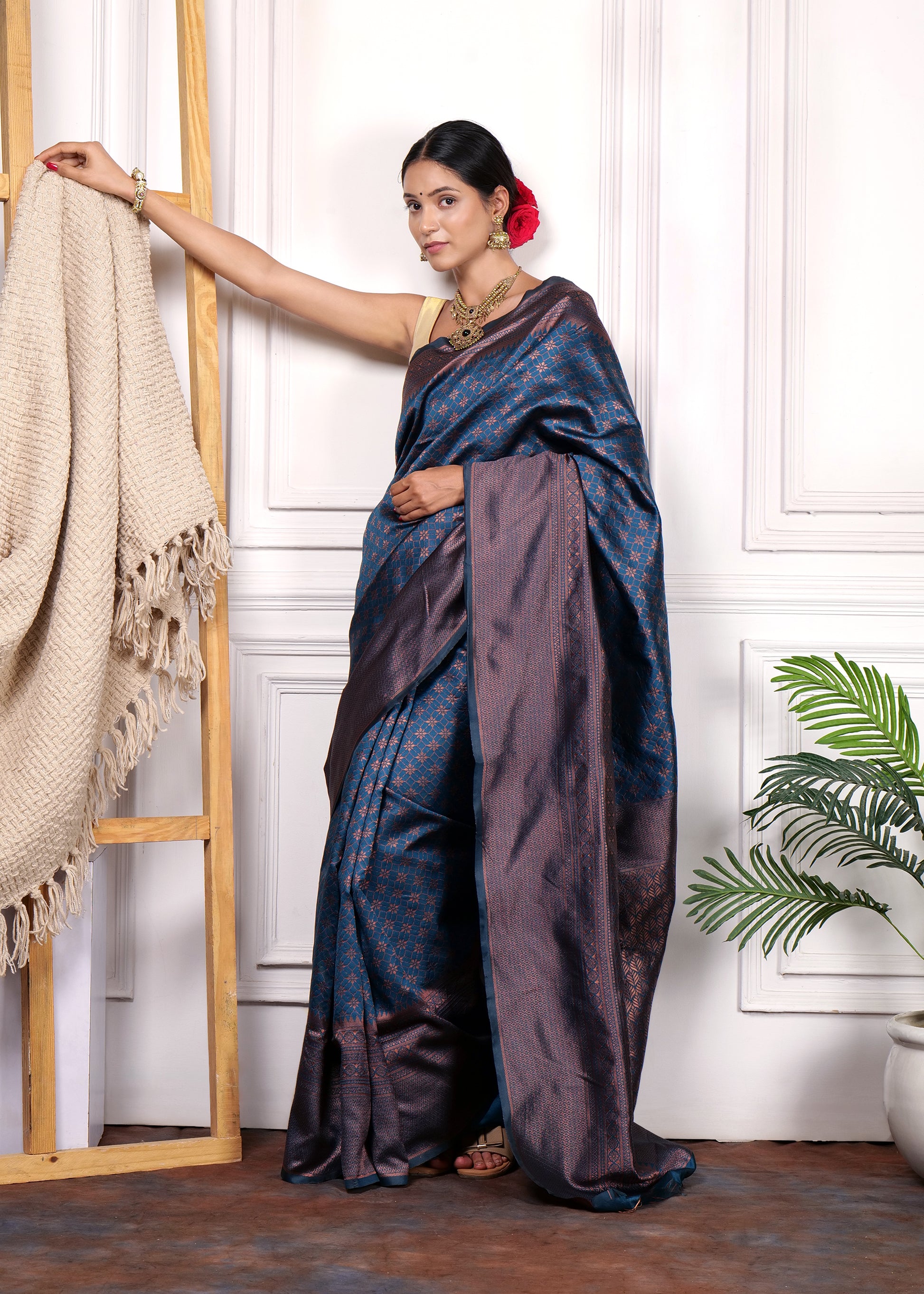 Side view of woman wearing a navy blue Kanjivaram silk saree with traditional jewelry and a red rose in her hair