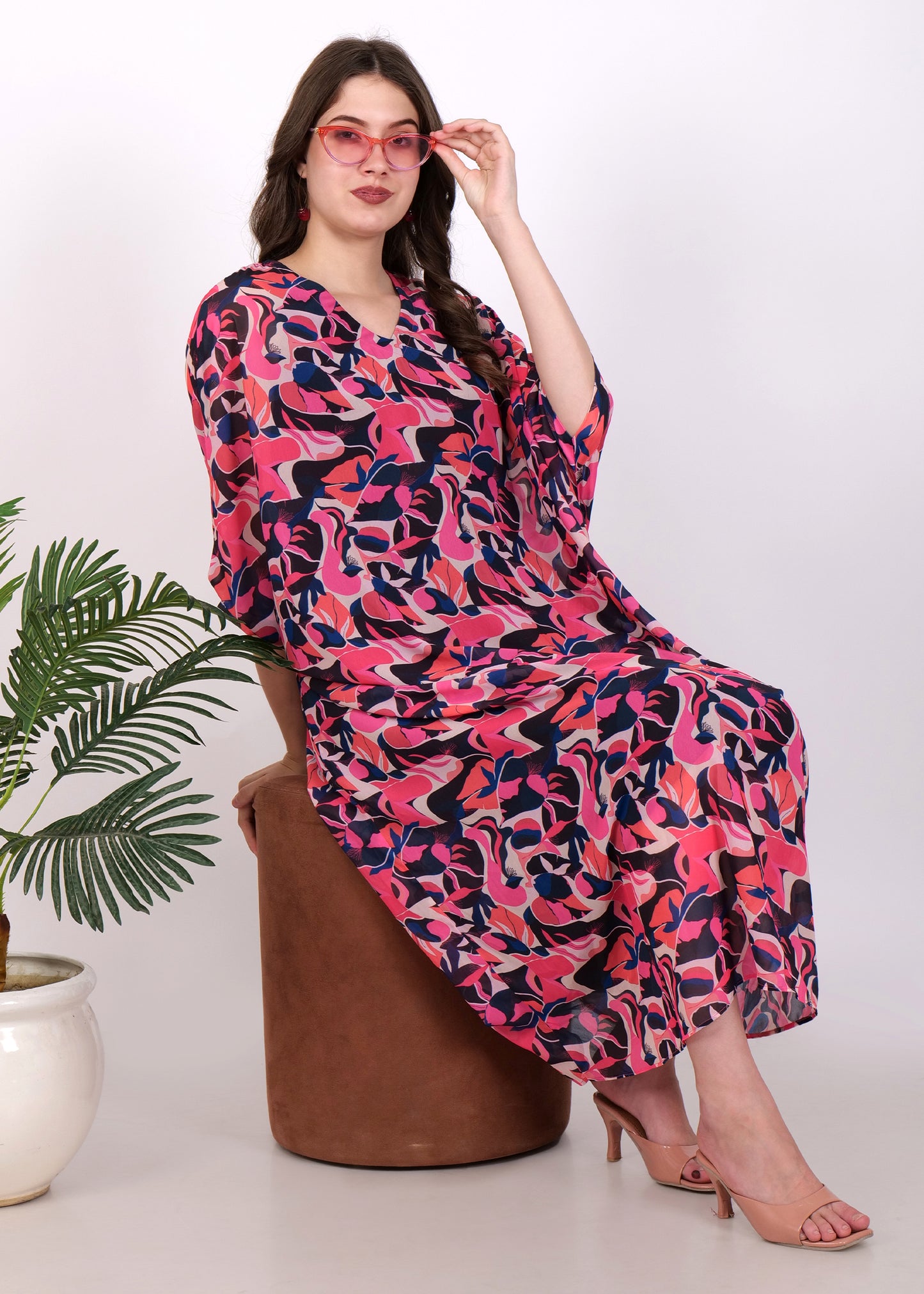 Model seated wearing a pink and purple abstract kaftan dress paired with trendy pink sunglasses, styled for a chic casual look