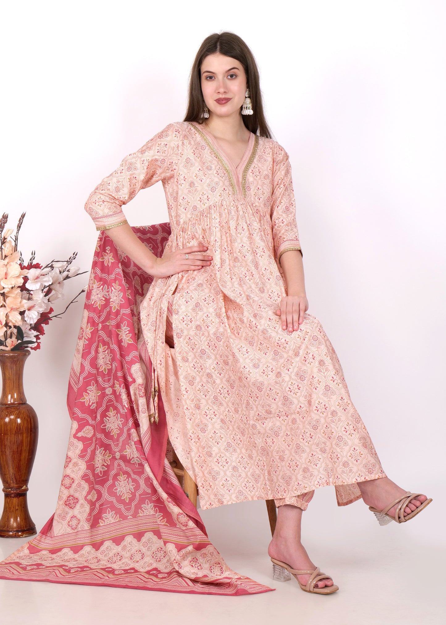  "Model wearing peach Anarkali suit with bold floral dupatta, paired with ethnic jewelry, perfect for festive wear."