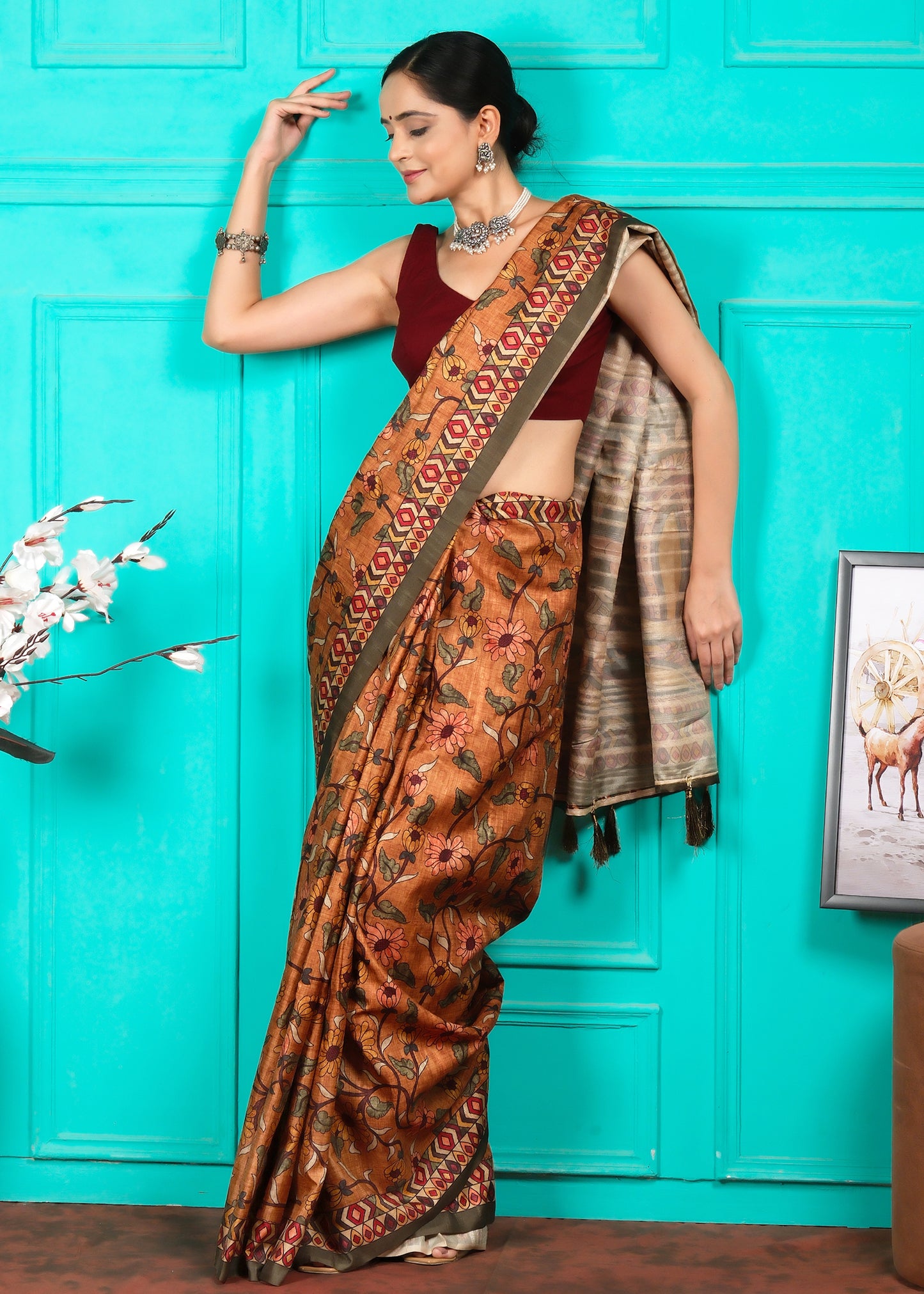 A side profile of a woman wearing a traditional handloom saree, showing the intricate floral patterns and geometric border. The turquoise wall contrasts beautifully with the earthy tones of the saree, highlighting the craftsmanship.