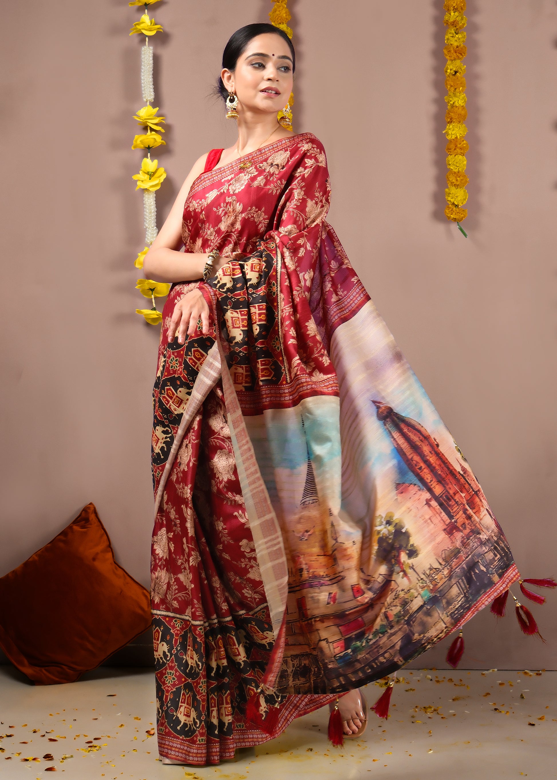 Woman gracefully showing off a red saree with temple and elephant motifs, adorned with festive marigold flowers.