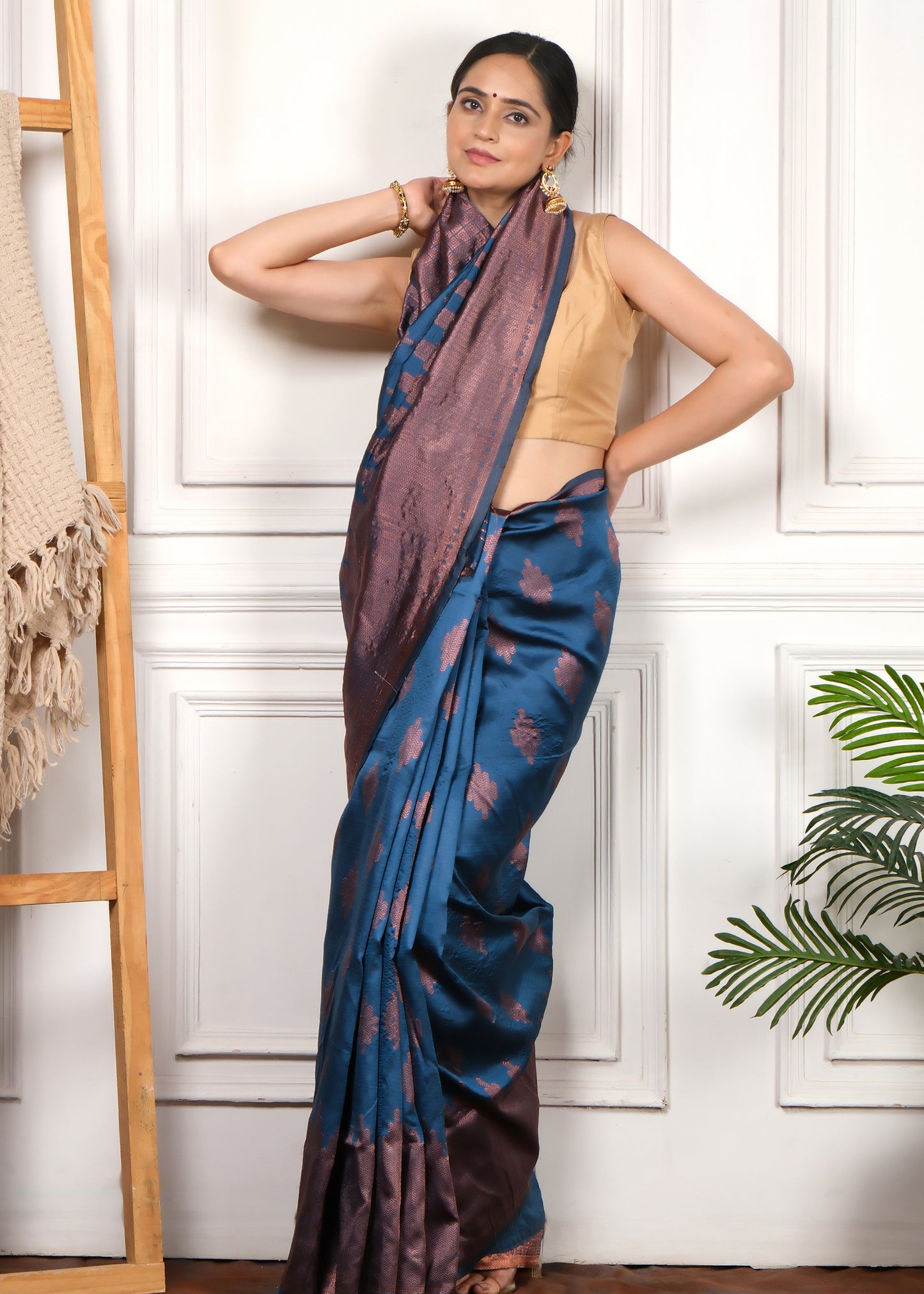 Model showcasing a royal blue silk saree with copper zari motifs, standing gracefully in a traditional setting